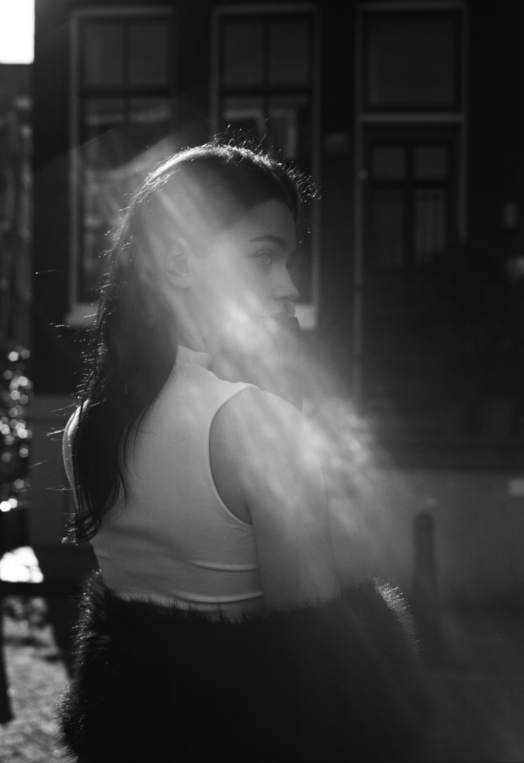 Portret op Fomapan 100 van een vrouw die over haar schouder kijkt, terwijl een streep licht over haar wang en haar haar valt