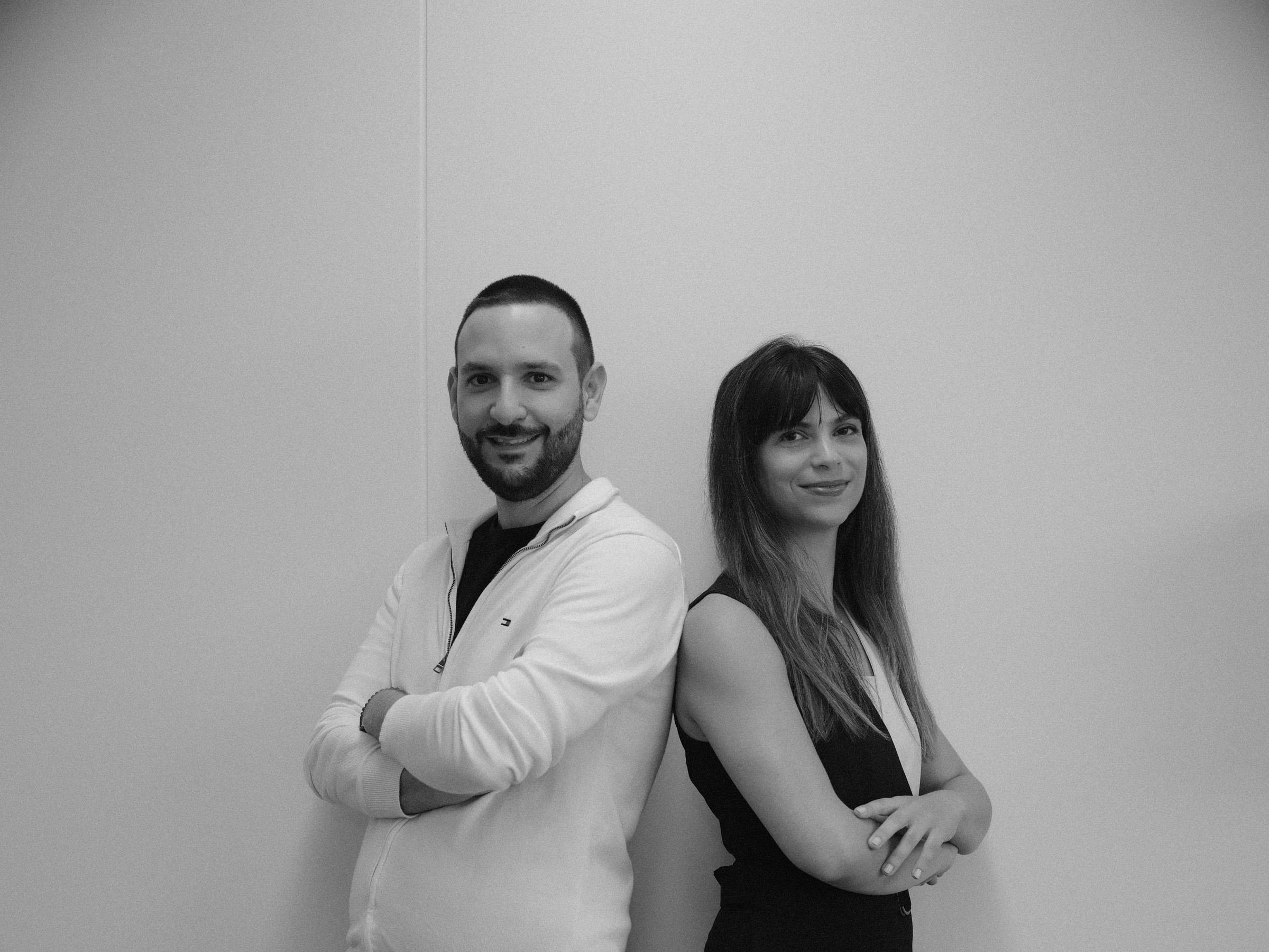 Black and white portrait of two psychologists standing back to back with crossed arms against a plain wall at their branding shoot