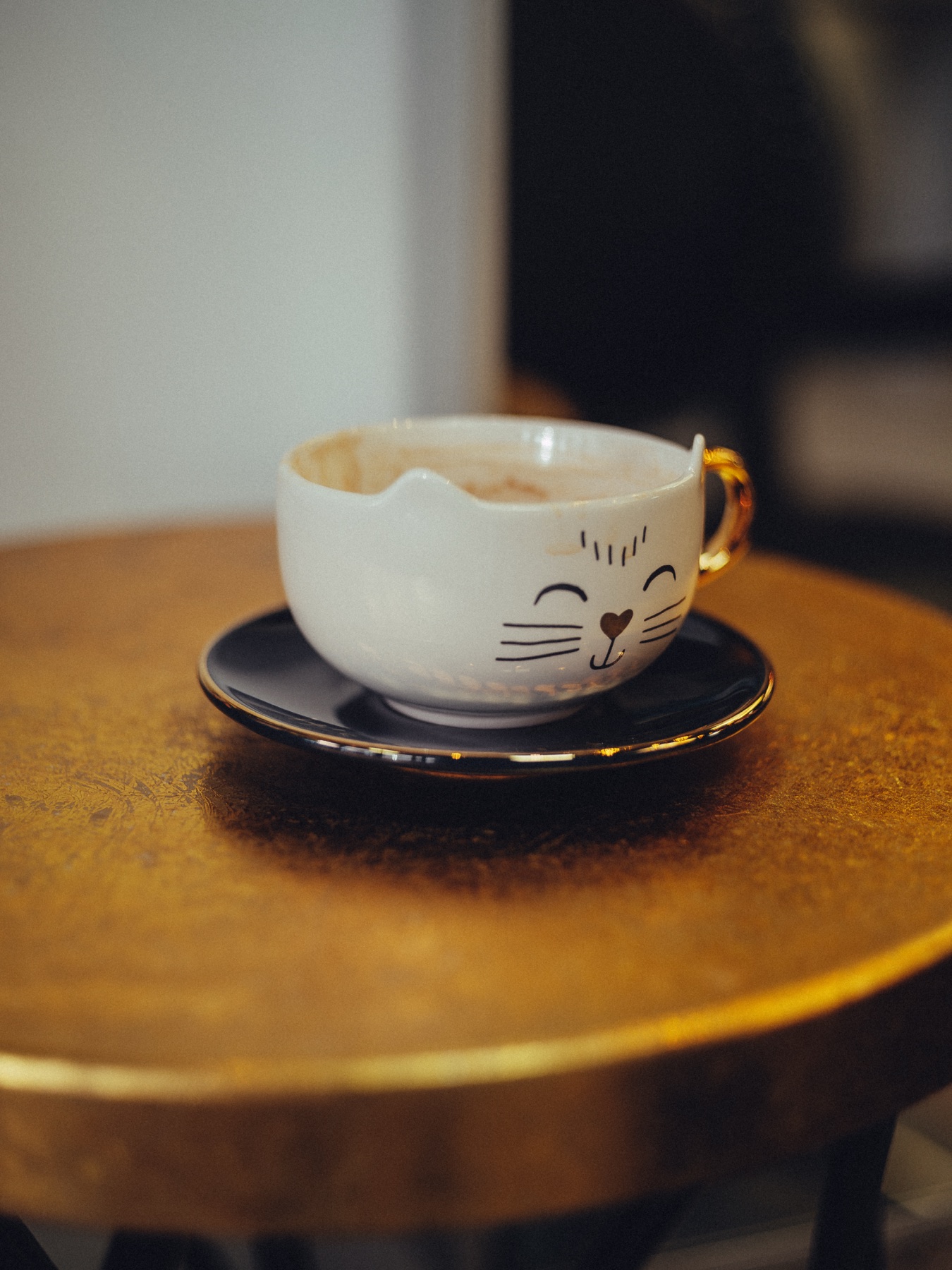 Koffie in een wit kopje met een lachend kattengezicht en een gouden oor, op een klein gouden bijzettafeltje