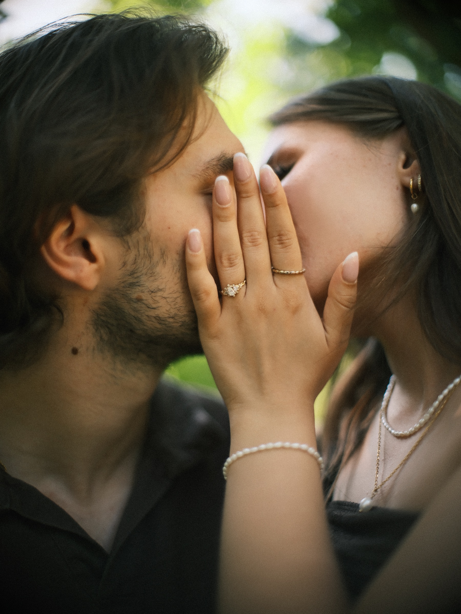 Close kiss on a garden bench, her hand with the new ring on his cheek and a thin bracelet of small pearls on her wrist