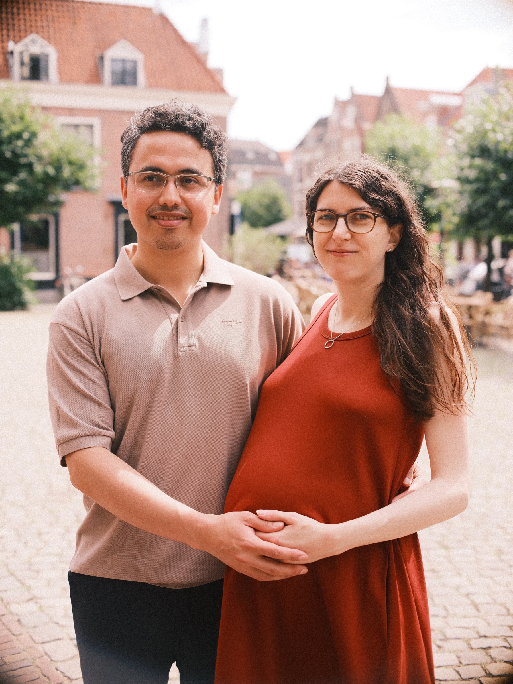 Close portrait of an expecting couple on a square in Leiden, his arms around her and their hands joined over her bump