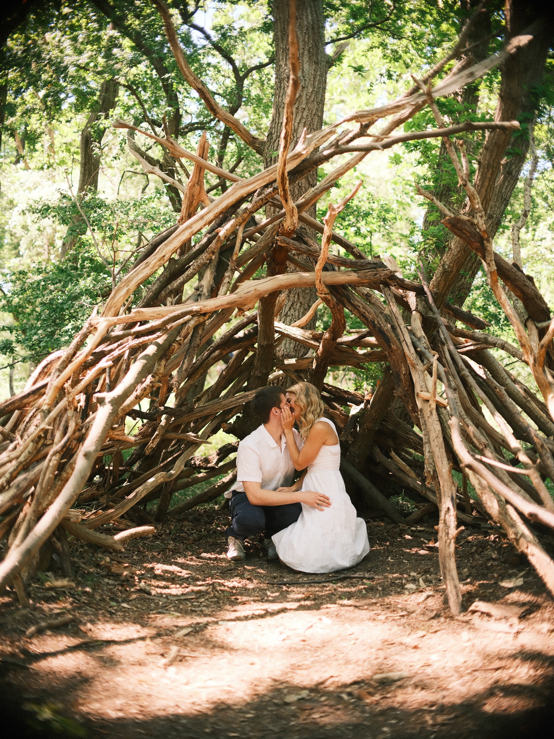 Stel kust in een hut van gebogen takken in het bos, de vrouw in het wit en de man geknield naast haar