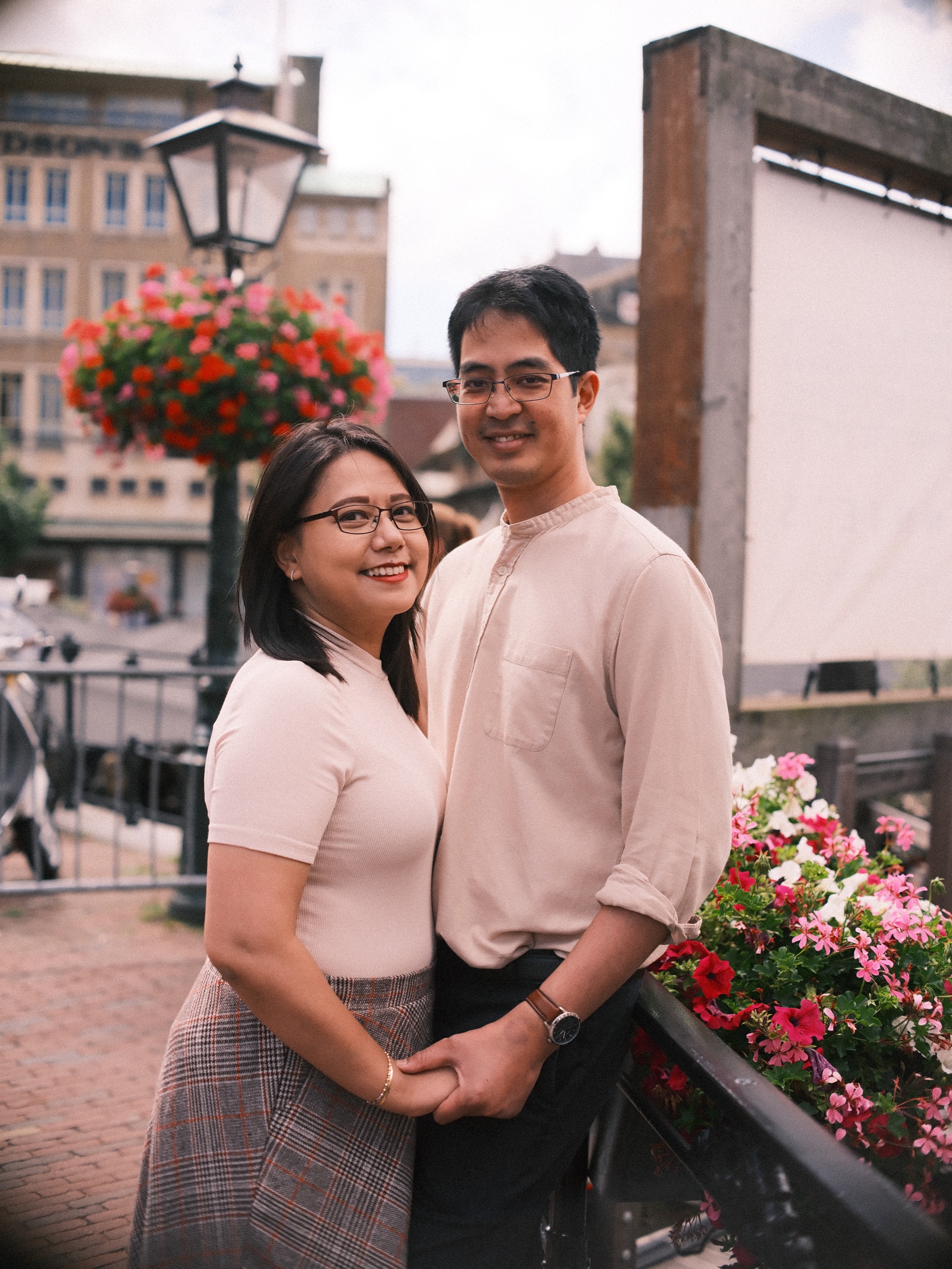 Close portrait of the couple holding hands by a railing over the water in Leiden, a lamppost with red flowers and pink blooms around them
