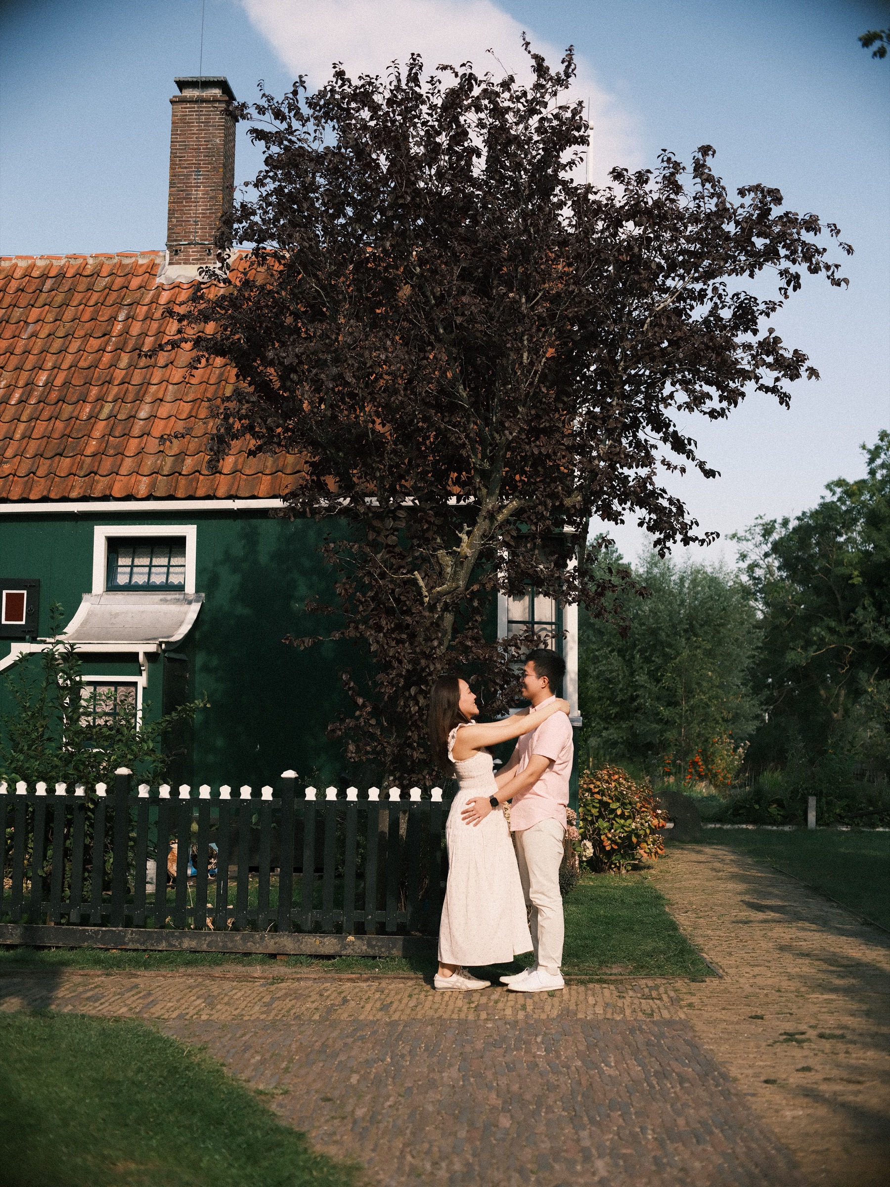 Couple embracing in front of a green wooden house with a red tile roof and a dark red-leaved tree at the Zaanse Schans