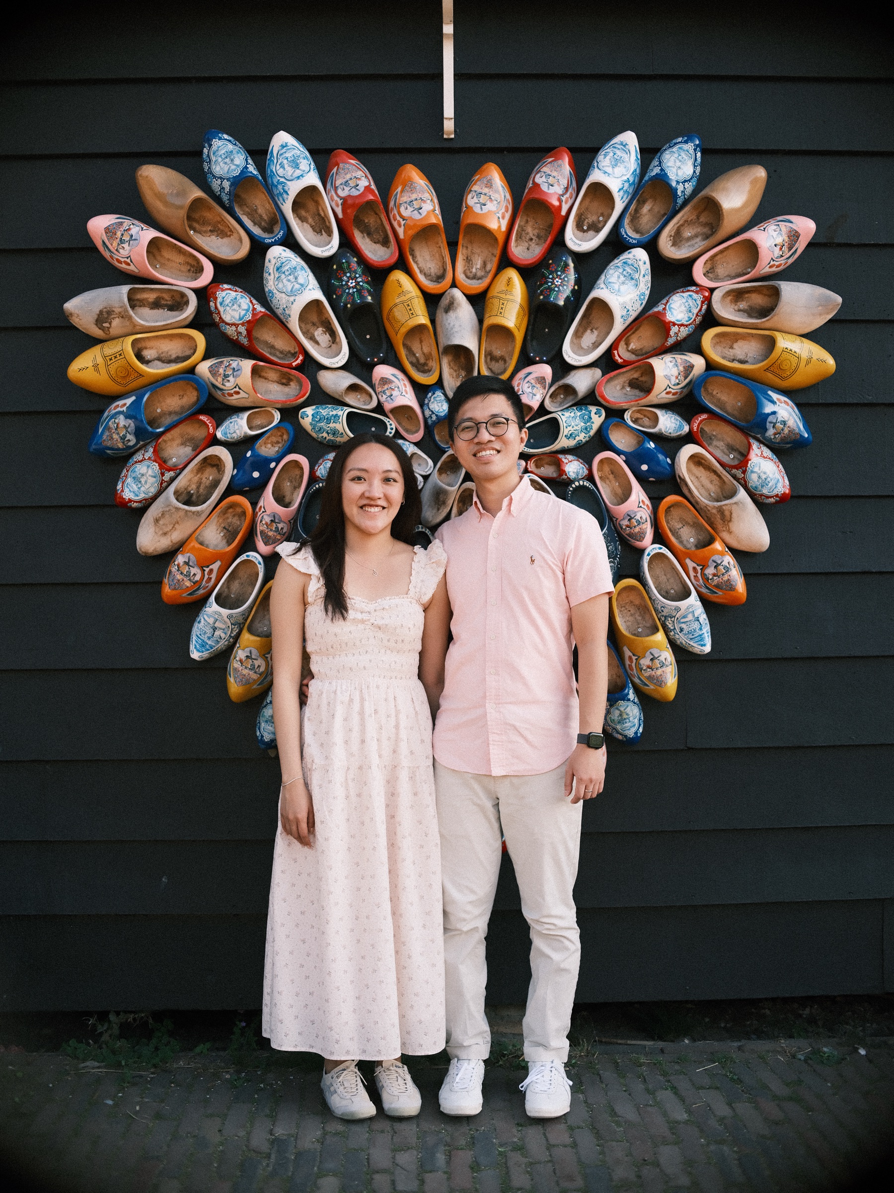 Couple standing in front of a big heart made of painted wooden clogs on a dark wooden wall at the Zaanse Schans