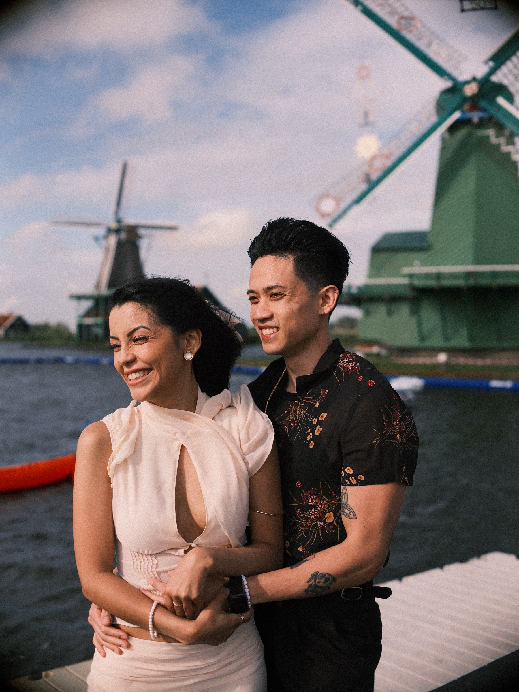 Woman laughing as her partner holds her from behind by the Zaan, a green windmill and red and white boats in the background