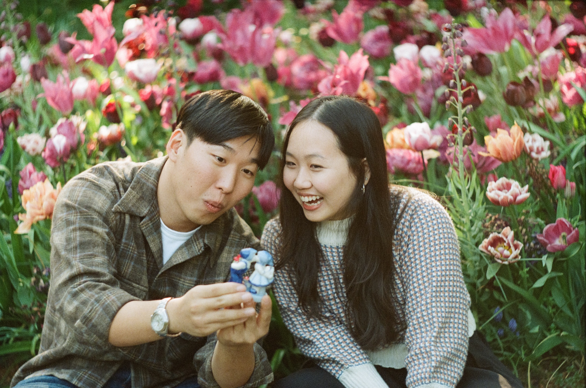 Couple laughing at a small blue-and-white figurine of a kissing Dutch couple after the proposal at Keukenhof