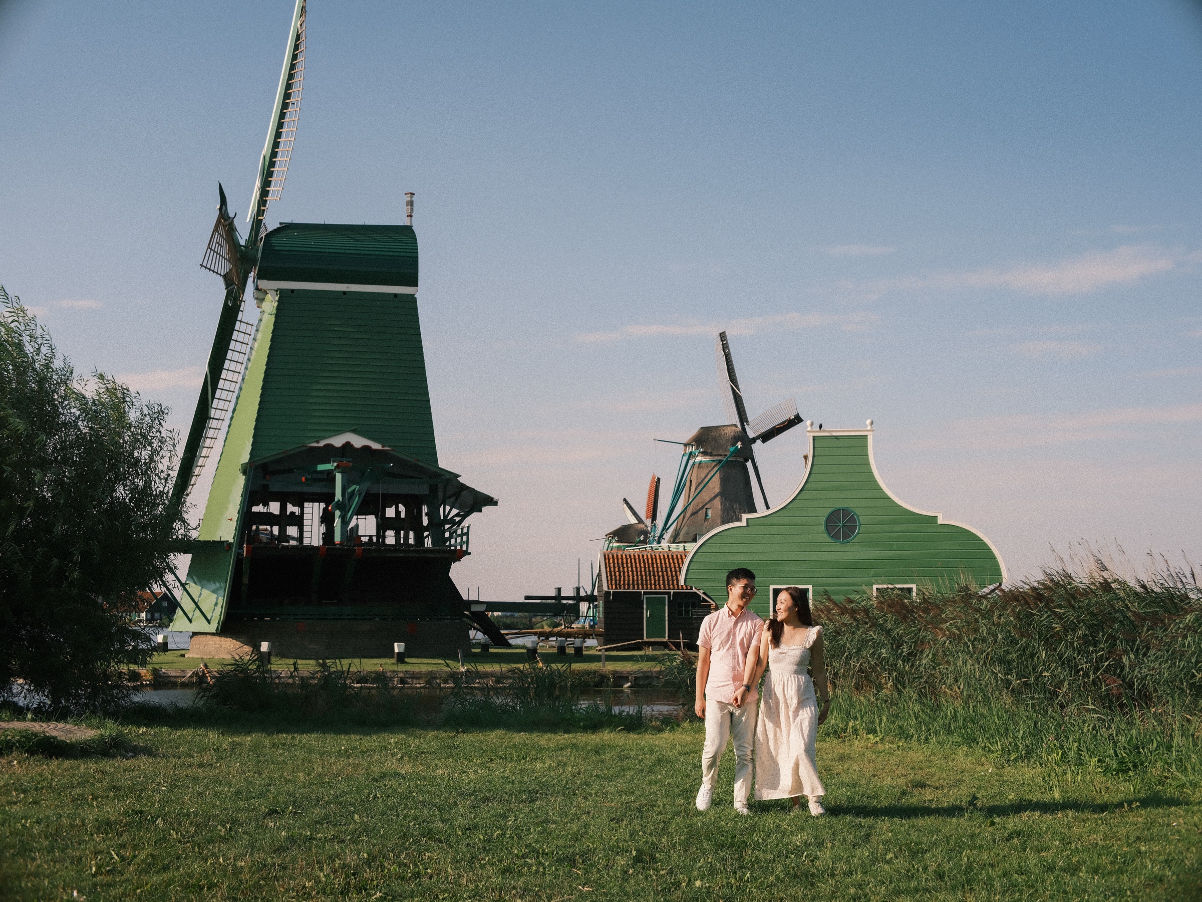 Wide view of the Zaanse Schans windmills over a green meadow, a couple small in the grass walking hand in hand