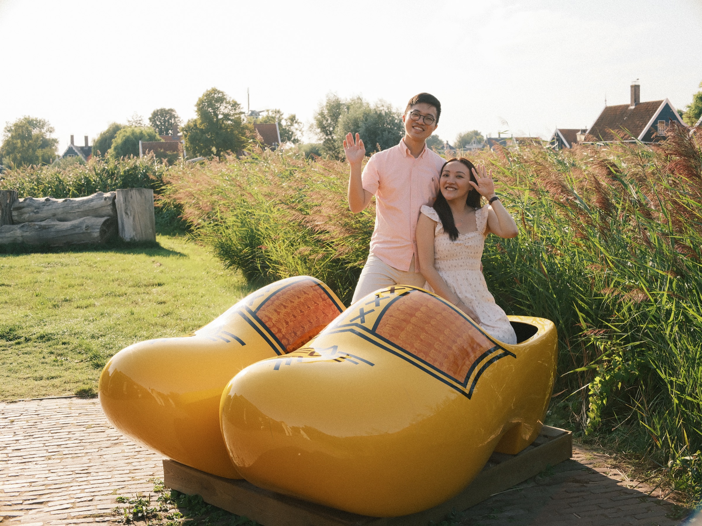 Couple sitting in a giant yellow clog in the reeds, the man waving and the woman laughing, a playful end to their engagement photos