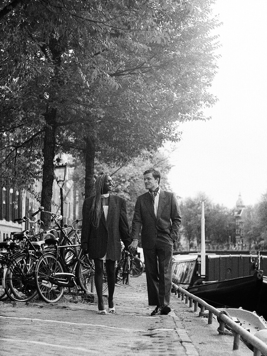 Walking hand in hand along an Amsterdam canal, a couple look at each other during their analog photoshoot