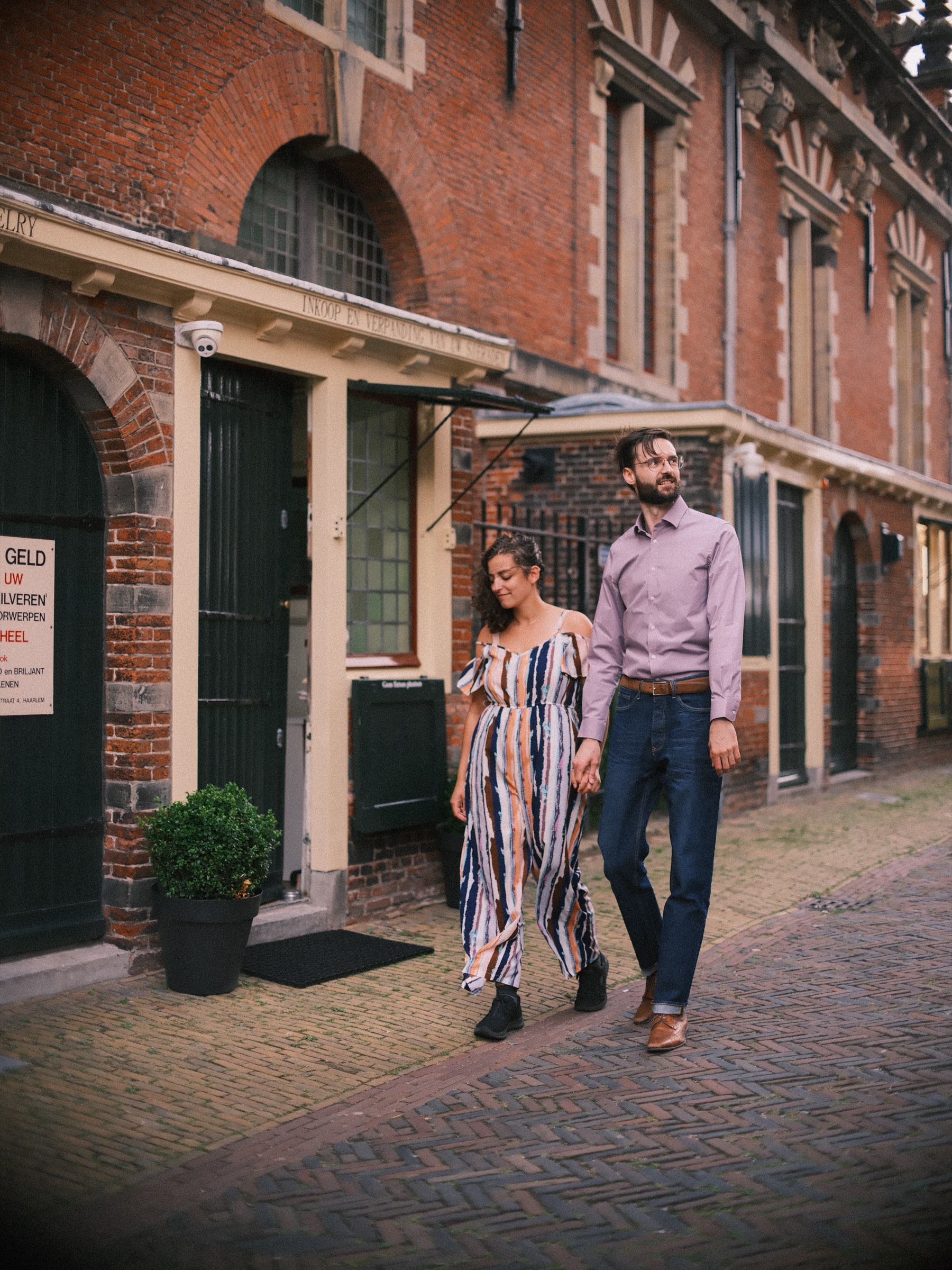 Stel loopt naast elkaar langs de sierlijke bakstenen gevels van de Vleeshal in Haarlem, op een bewolkte middag in de zomer