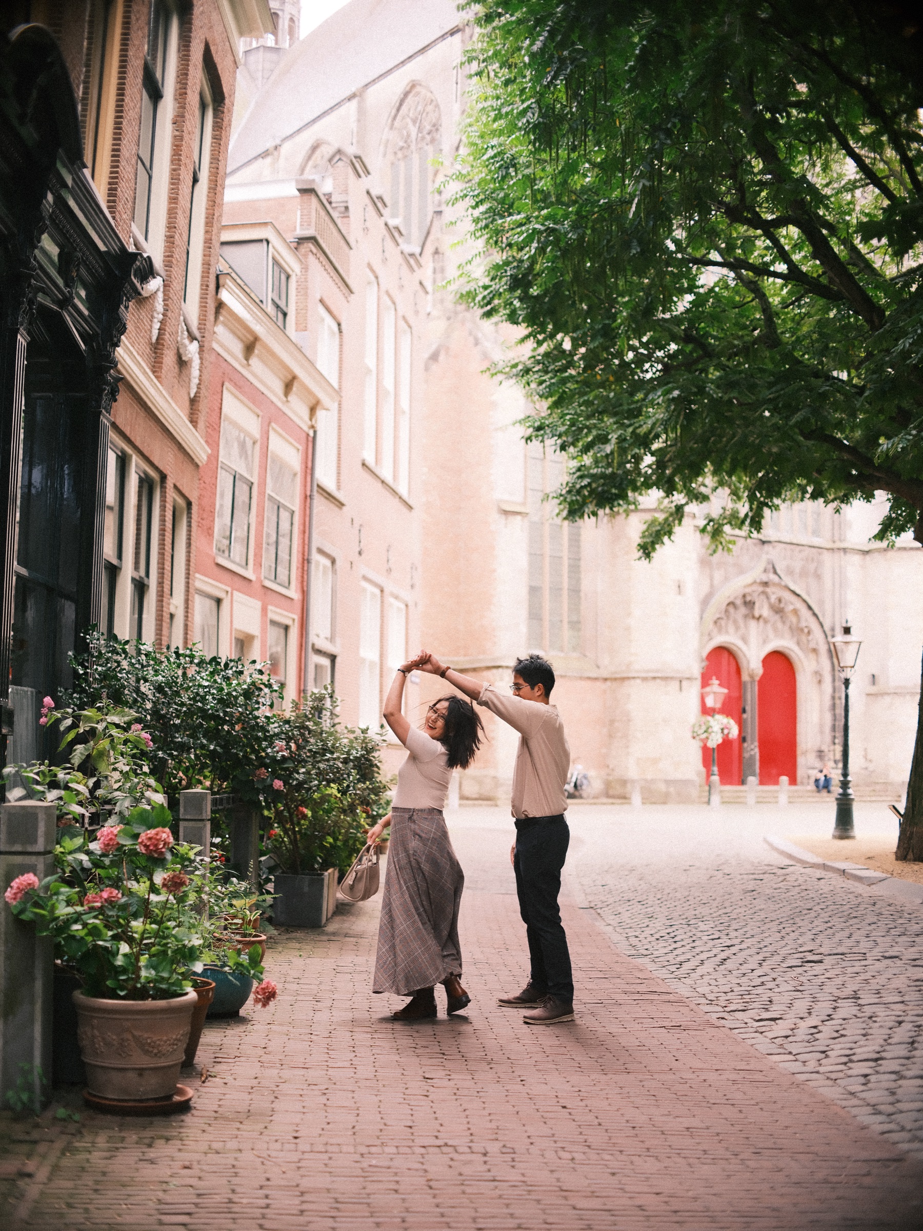 Couple dancing in a quiet Leiden street, his arm raised as she turns, the red doors of the Pieterskerk at the far end