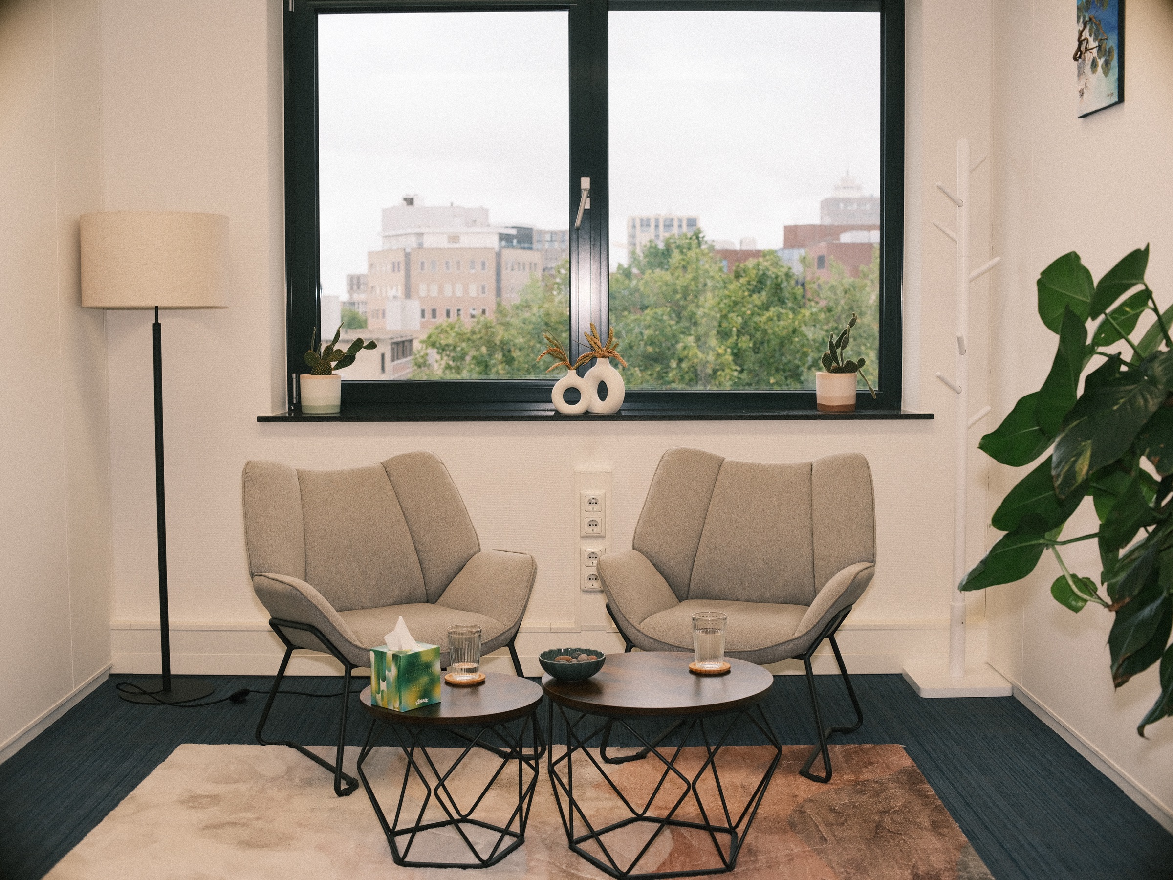 Empty room of the therapy practice with two gray armchairs, a tissue box on a small table, a floor lamp and a window over treetops