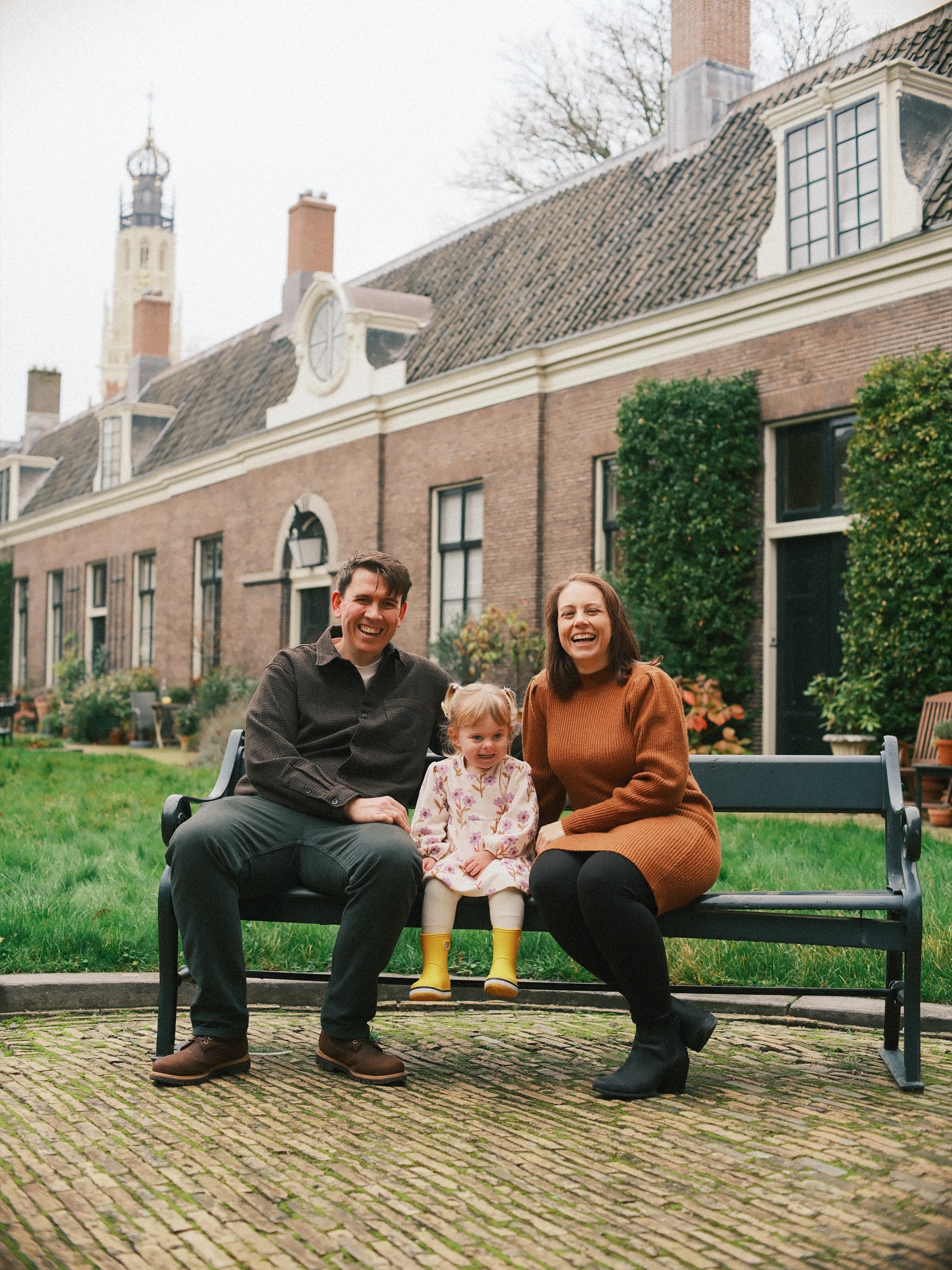 Lachend zit het gezin op een donkergroen bankje in Teylers Hofje in Haarlem, met lage bakstenen huisjes en de toren van de Bakenesserkerk