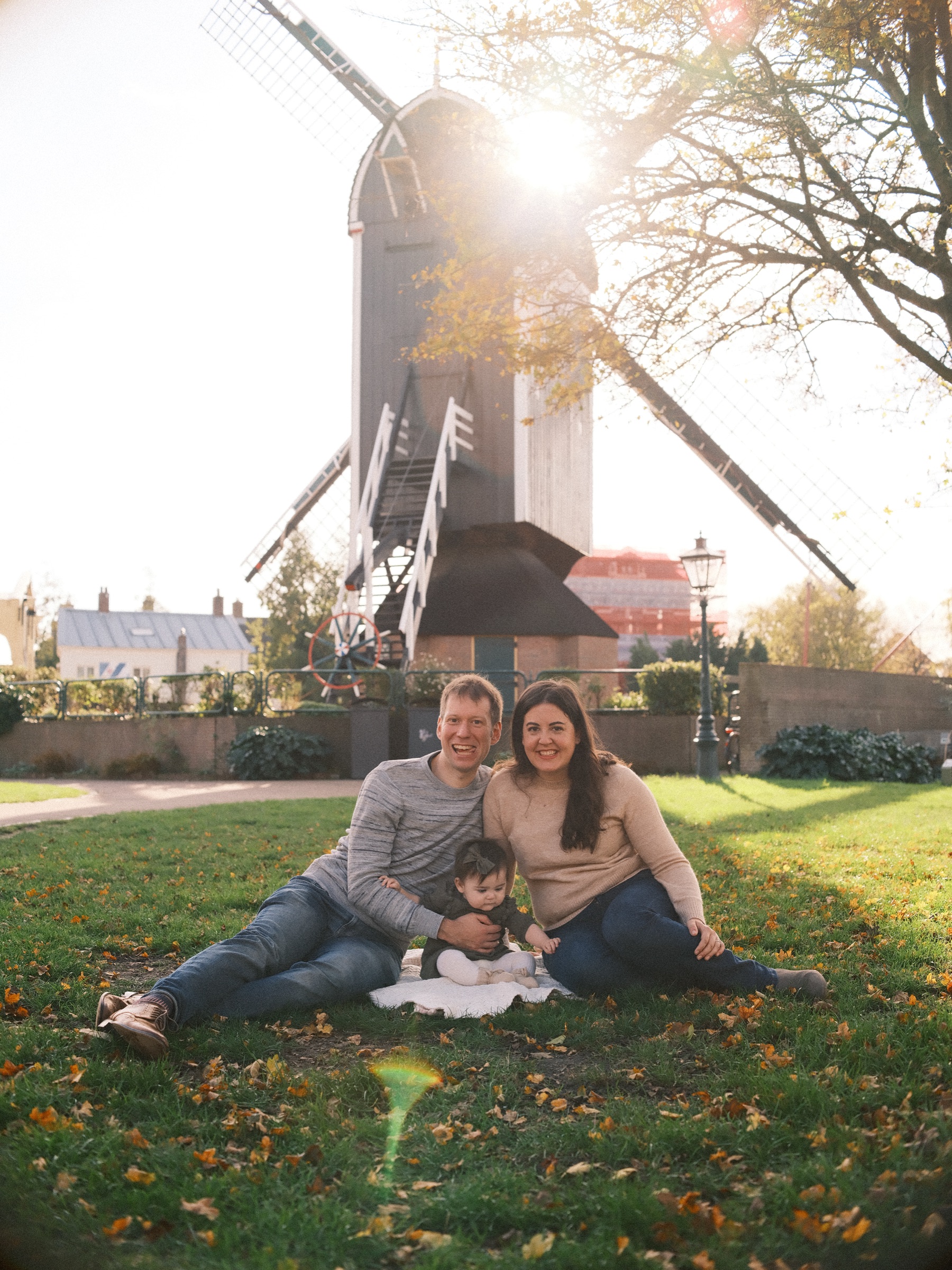 Family sitting on the grass below Molen De Put as the low sun breaks past the mill, fallen autumn leaves around their blanket