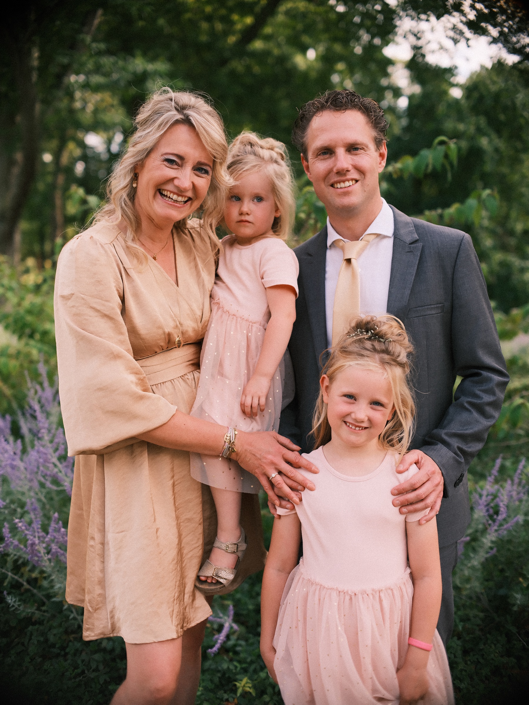 Vrouw in een roze satijnen jurk met haar dochtertje op de arm, naast een man in een grijs pak en een ouder meisje