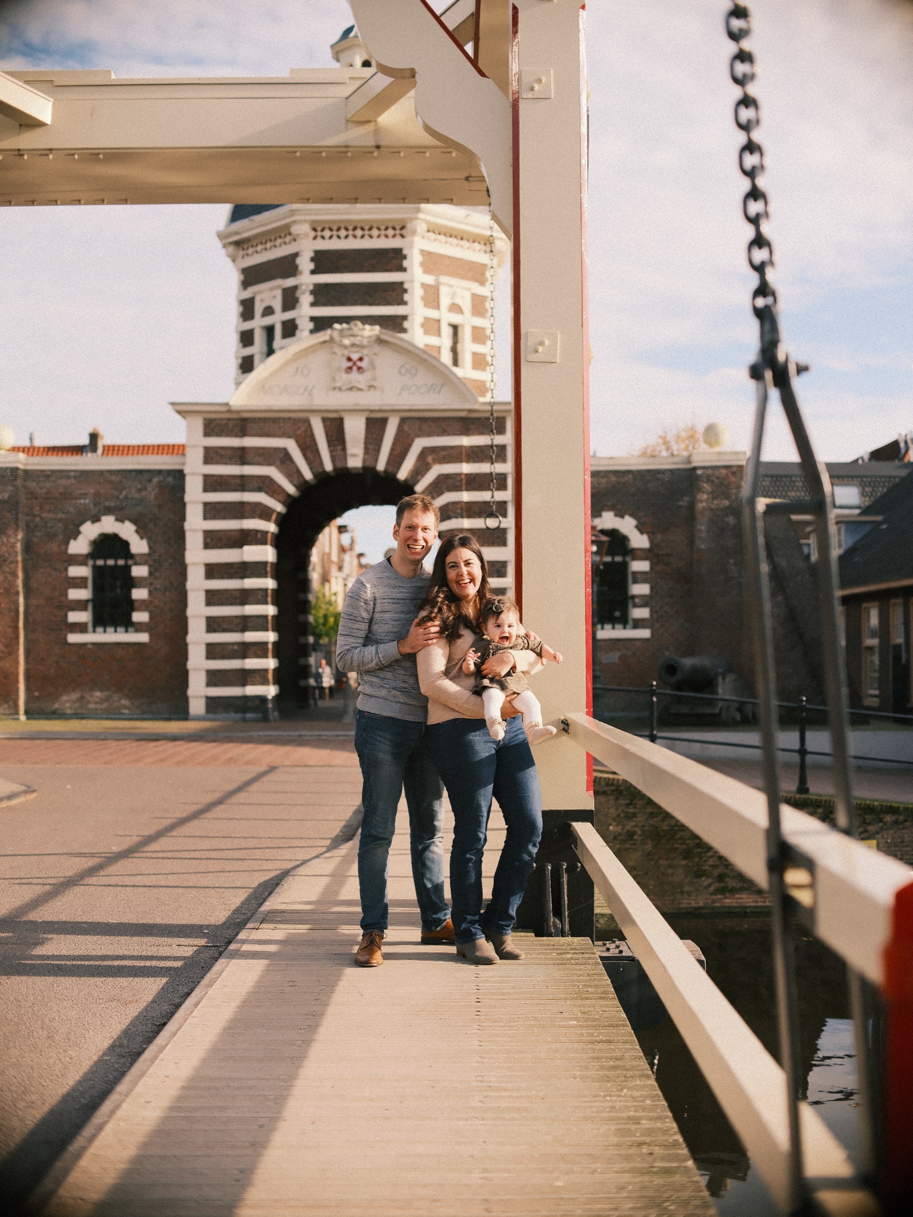Family on the white drawbridge before the Morspoort, an old city gate and photo spot in Leiden, its striped arch and dome in the autumn sun