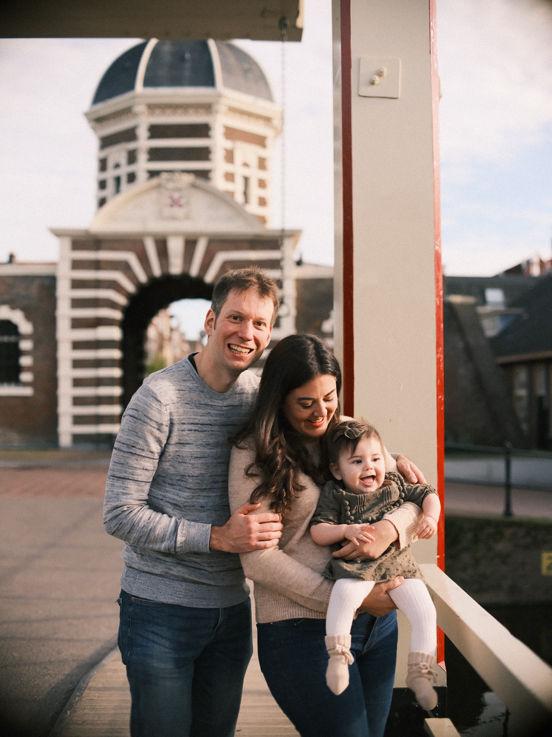 Parents and their baby daughter laughing on the white drawbridge in front of the Morspoort in Leiden, autumn sun on its dome