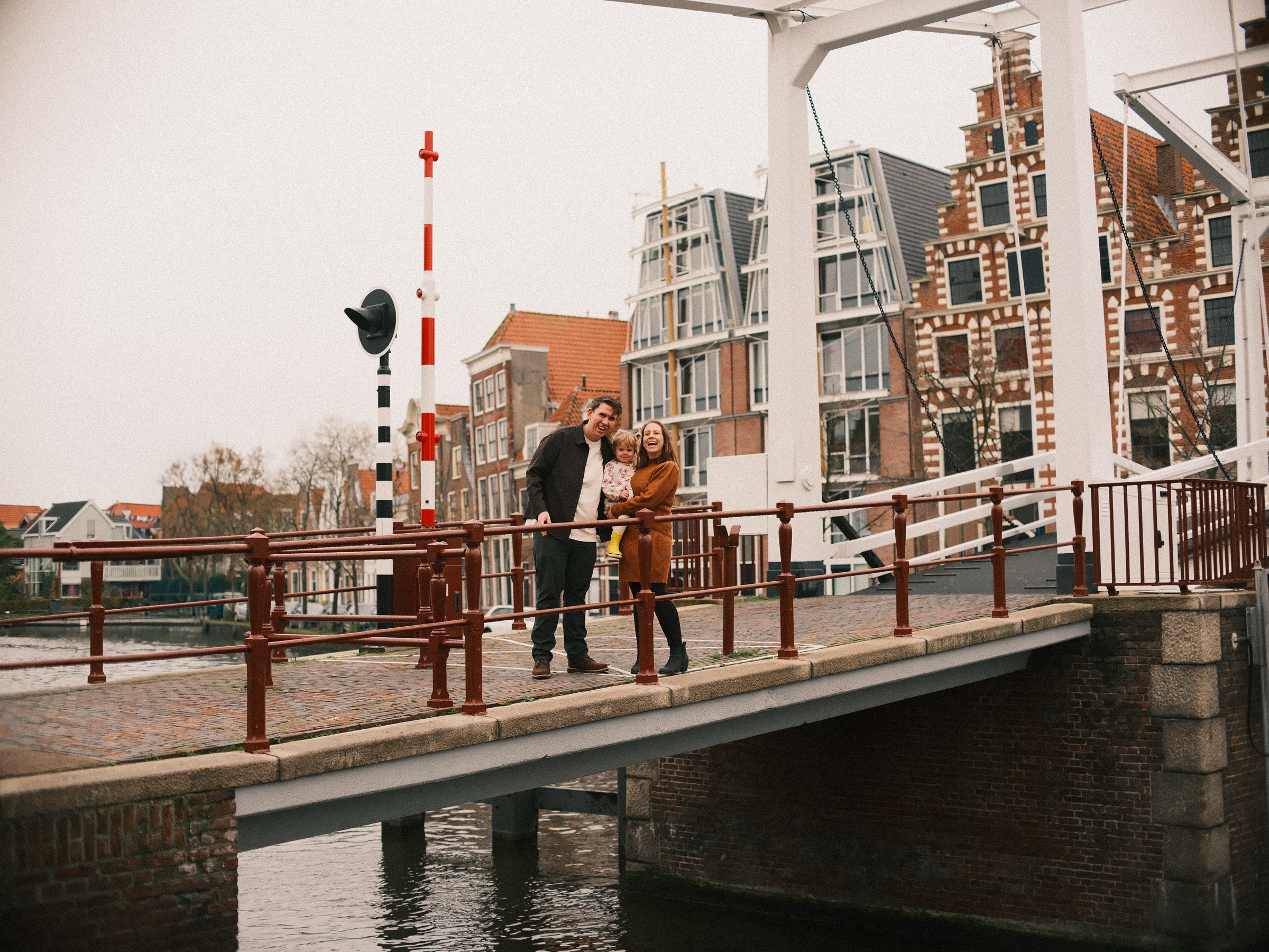 De witte Gravestenenbrug over het Spaarne met roodbruine leuningen, een hoge trapgevel erachter en een gezin halverwege de brug in Haarlem