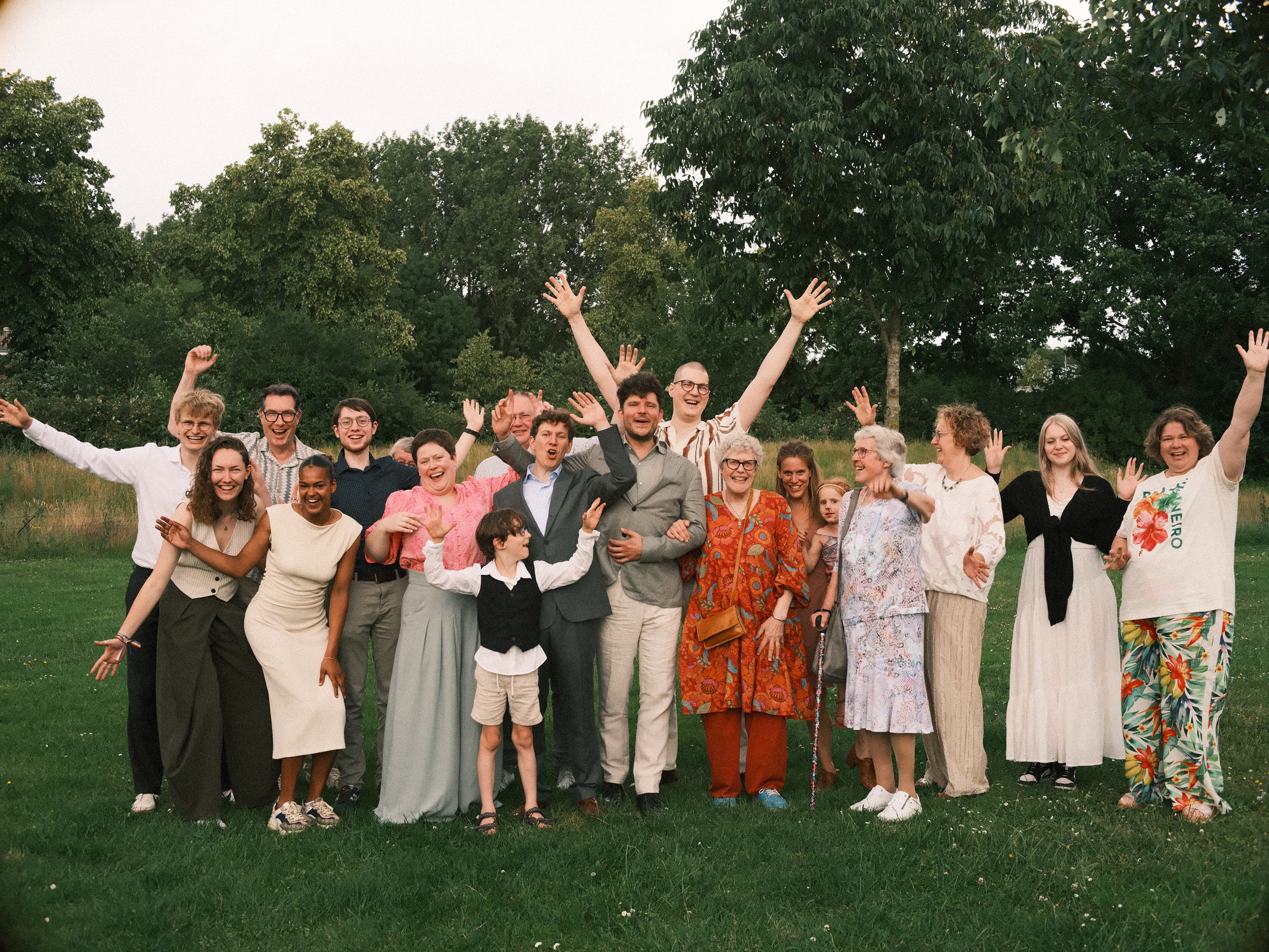 Wedding guests and family cheering with their arms in the air for a group photo on the grass in Utrecht, both grooms in the middle