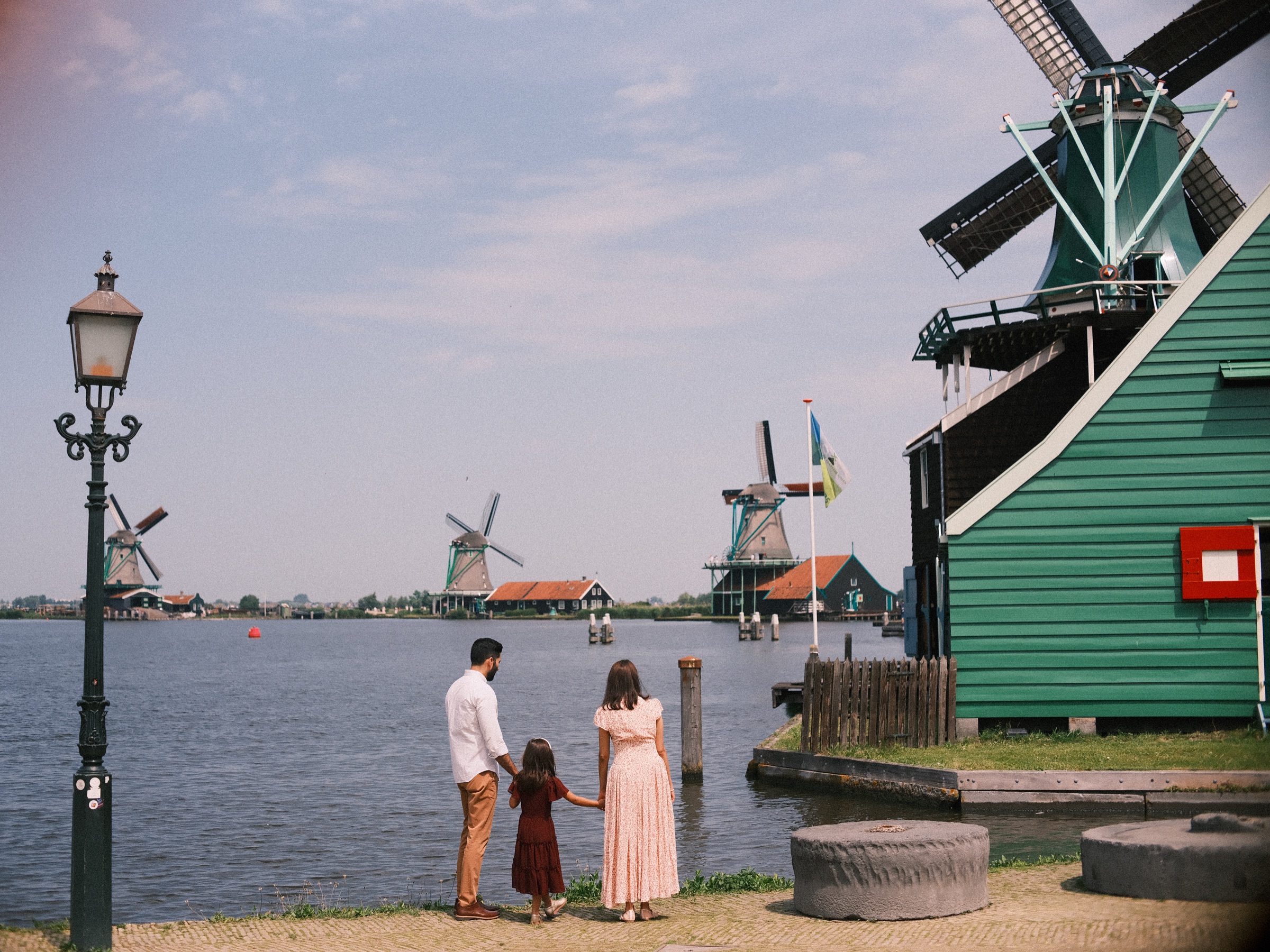 Family of three seen from behind on the quay by an old lamppost, looking out over the Zaan at the windmills of the Zaanse Schans
