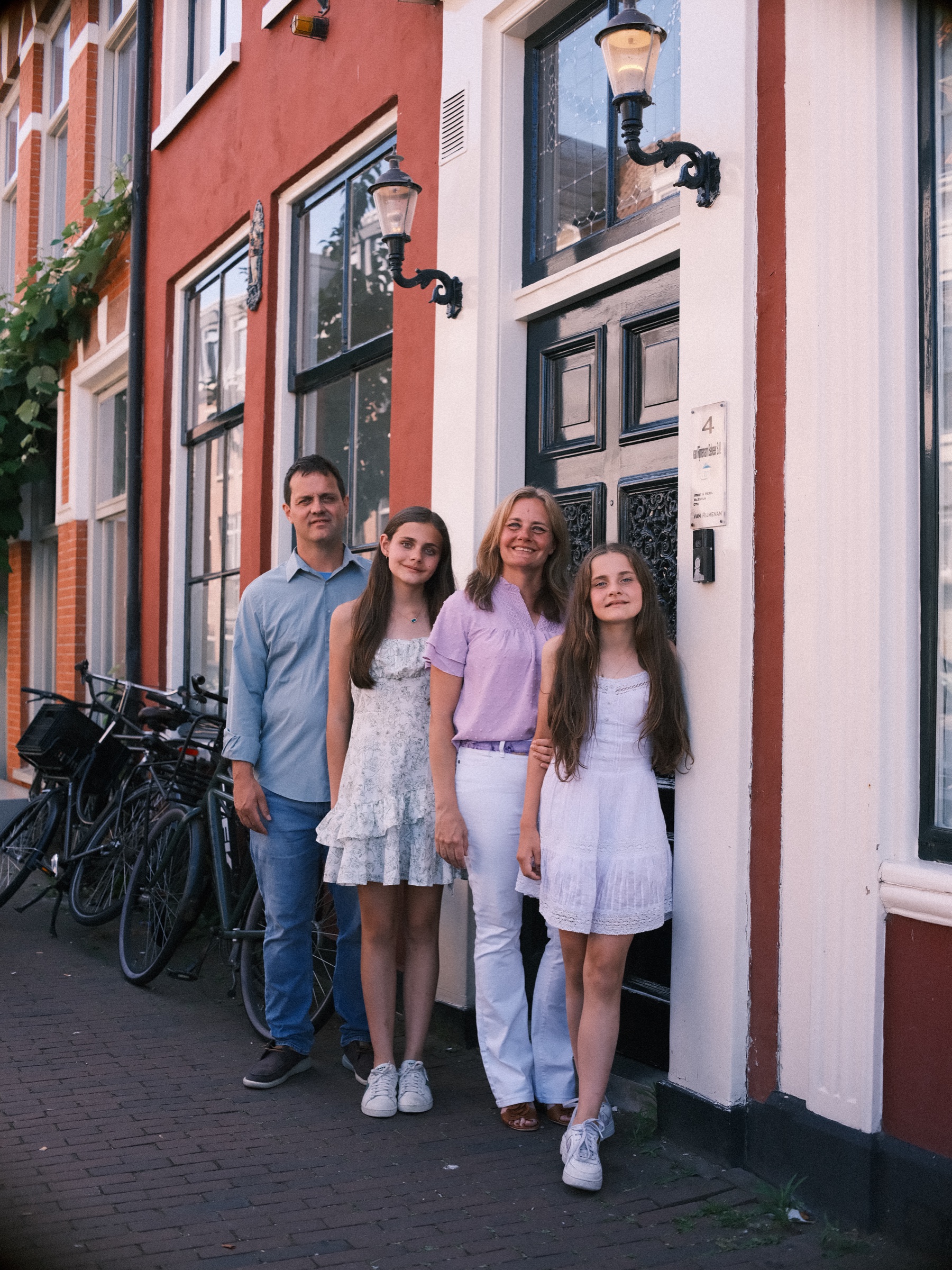 Ouders en twee dochters in het wit bij een rood-witte gevel met oude lantaarns en geparkeerde fietsen, in de oude binnenstad van Haarlem