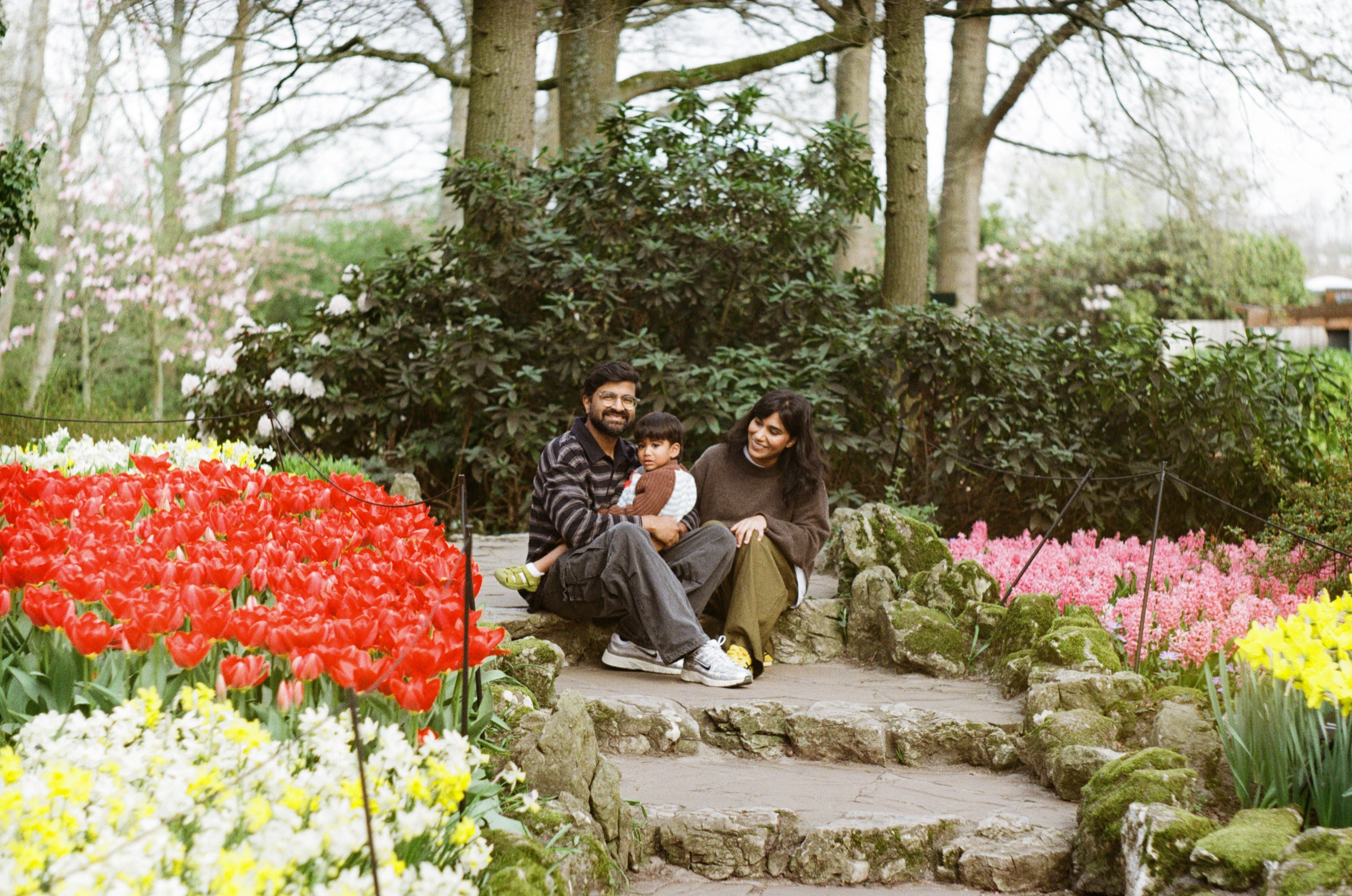 Family sitting on old stone steps in a rock garden, surrounded by red, pink and yellow tulips at Keukenhof