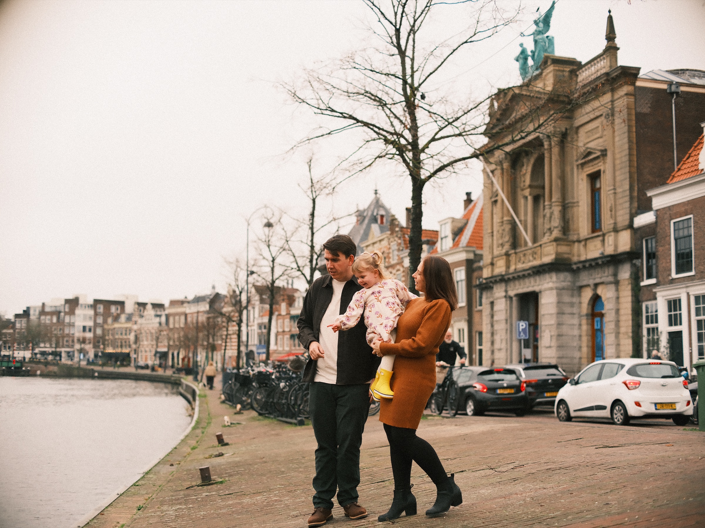 Gezin op de kade aan het Spaarne voor het Teylers Museum in Haarlem, de peuter wijst vanaf moeders arm naar het water