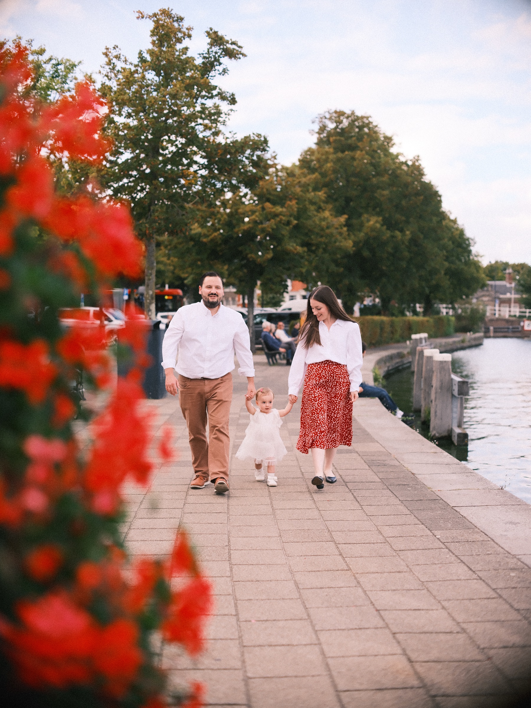 Gezin wandelt over de kade langs het water in Haarlem, het meisje zet stapjes tussen haar ouders, met rode geraniums vooraan
