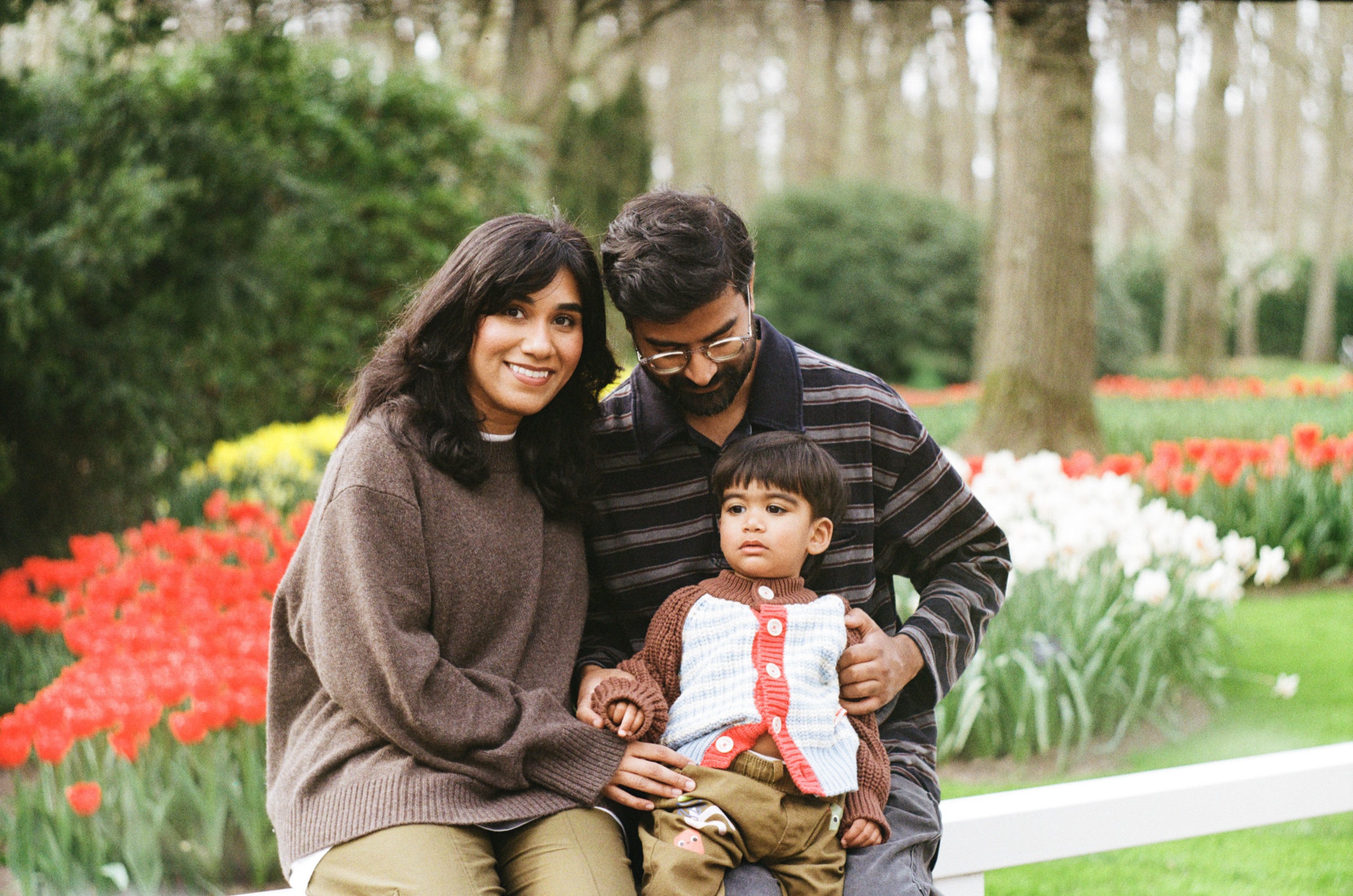Family of three on a white railing at Keukenhof, red and white tulips around them and the toddler sitting between his parents, on Kodak Gold 200