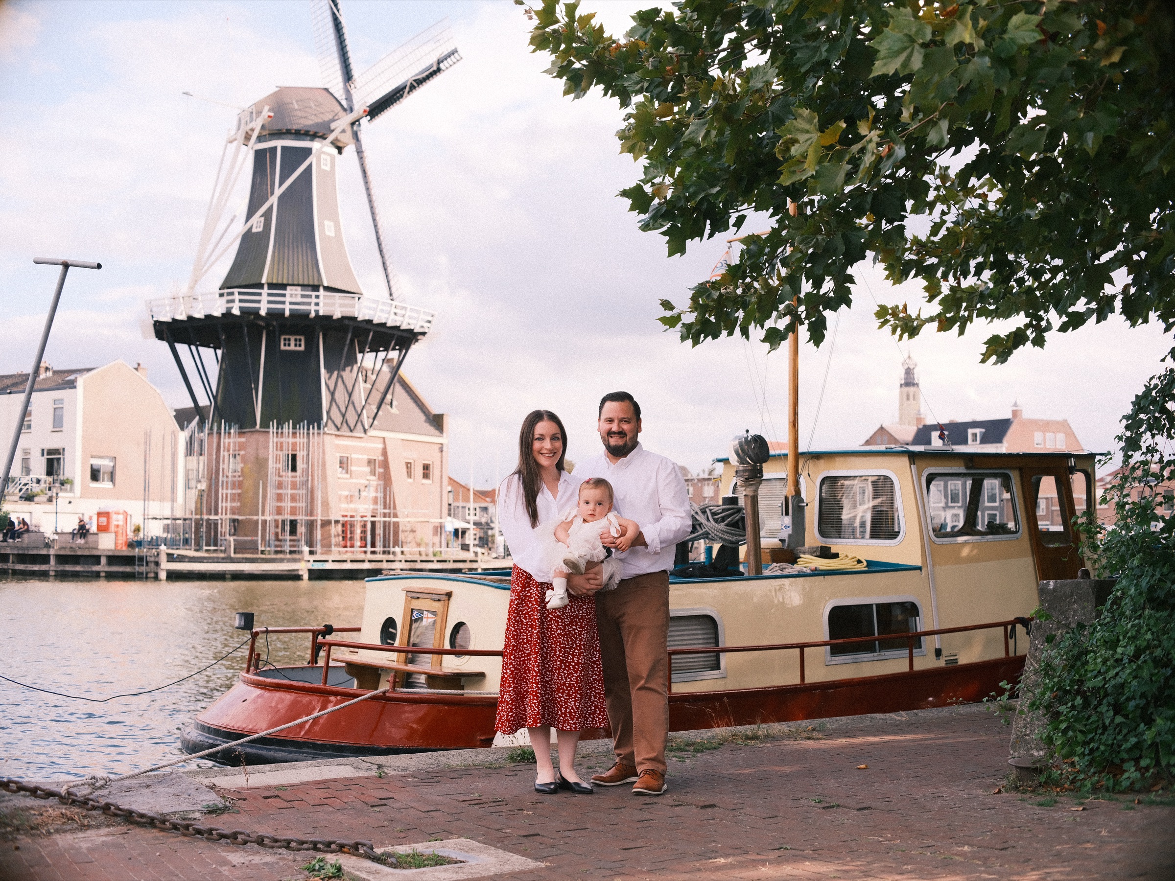 Jong gezin naast een klein houten bootje aan het Spaarne in Haarlem, met molen De Adriaan hoog boven hen