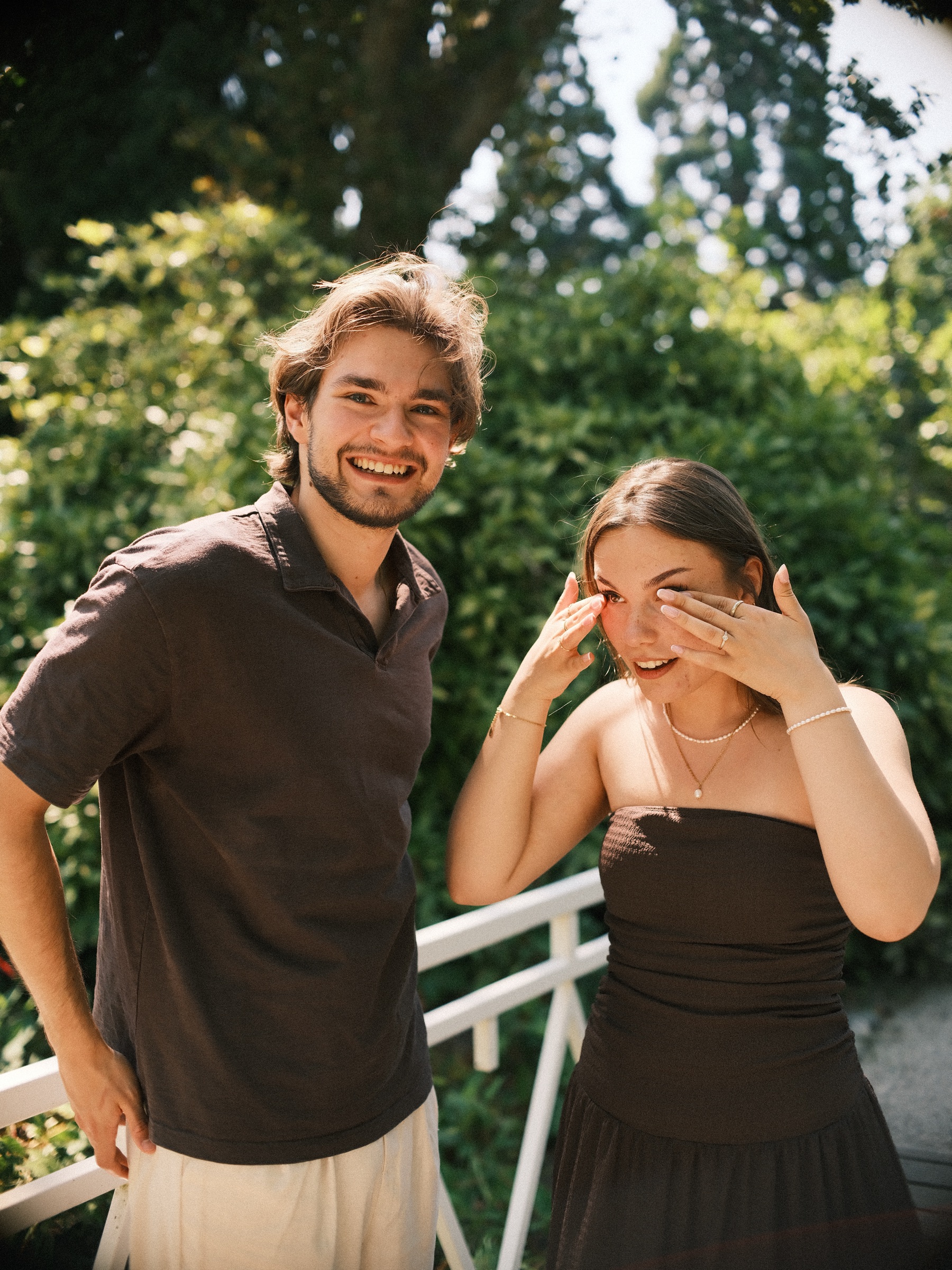 Laughing, she wipes a tear from her eye beside him on the bridge, just after saying yes to the proposal at Trompenburg