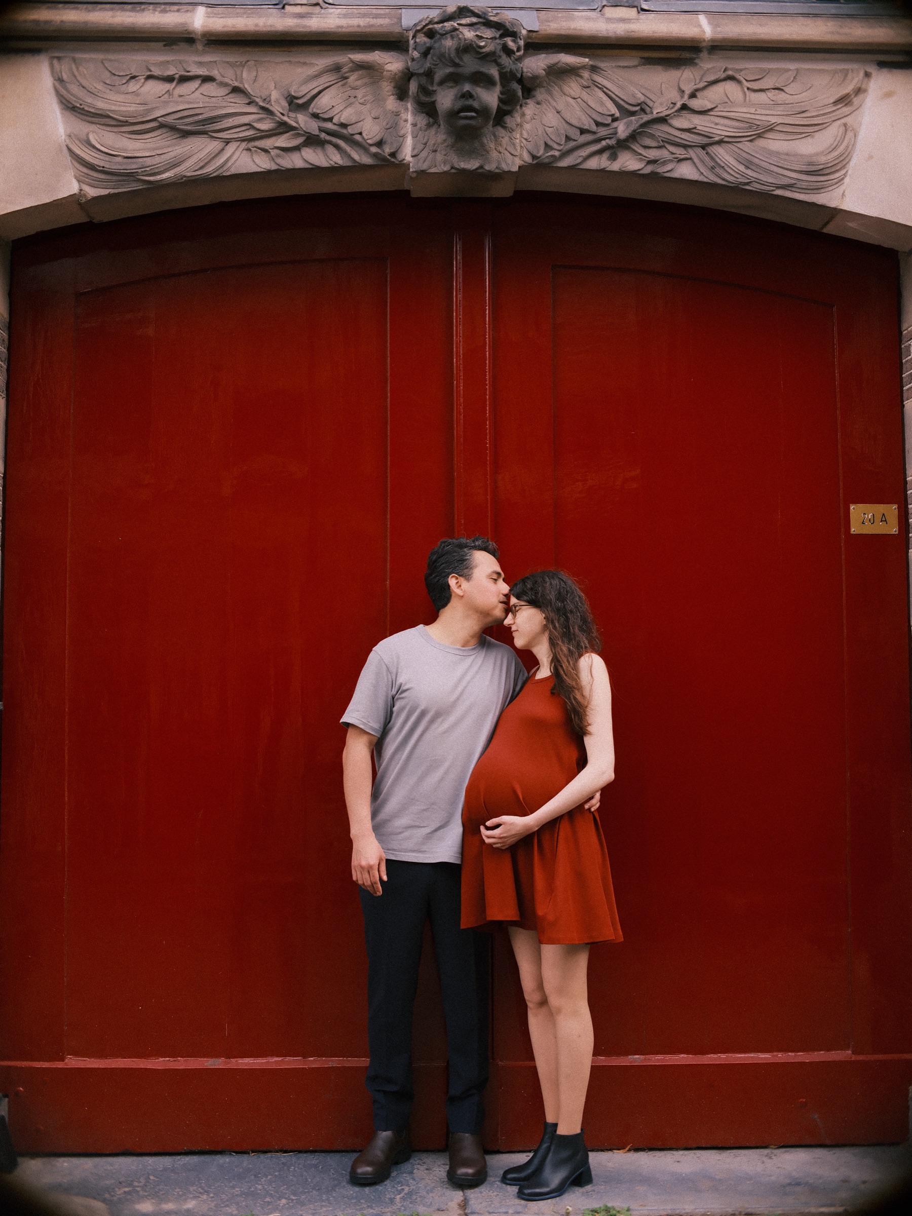 He kisses her forehead and she closes her eyes against a red door, one hand under her bump and his hand on her waist