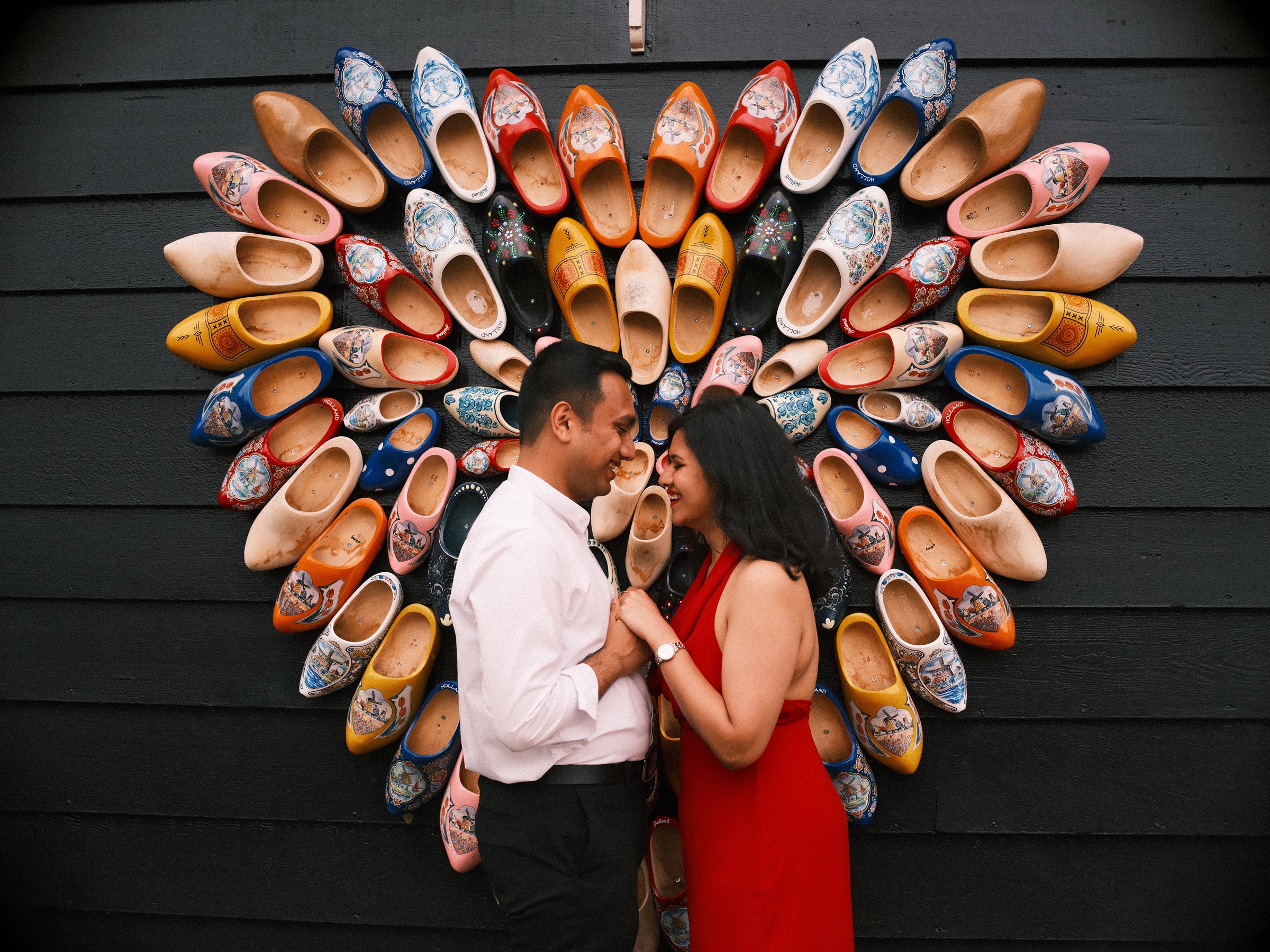 Couple touching foreheads in front of a big heart of painted wooden clogs on a dark wall at the Zaanse Schans