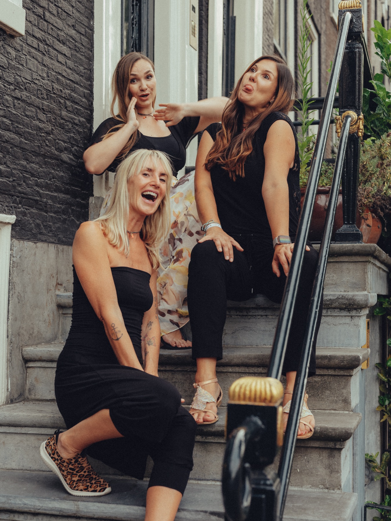 Bachelorette party friends pulling funny faces on the steps of a stoop, leopard sneakers and a black and gold railing