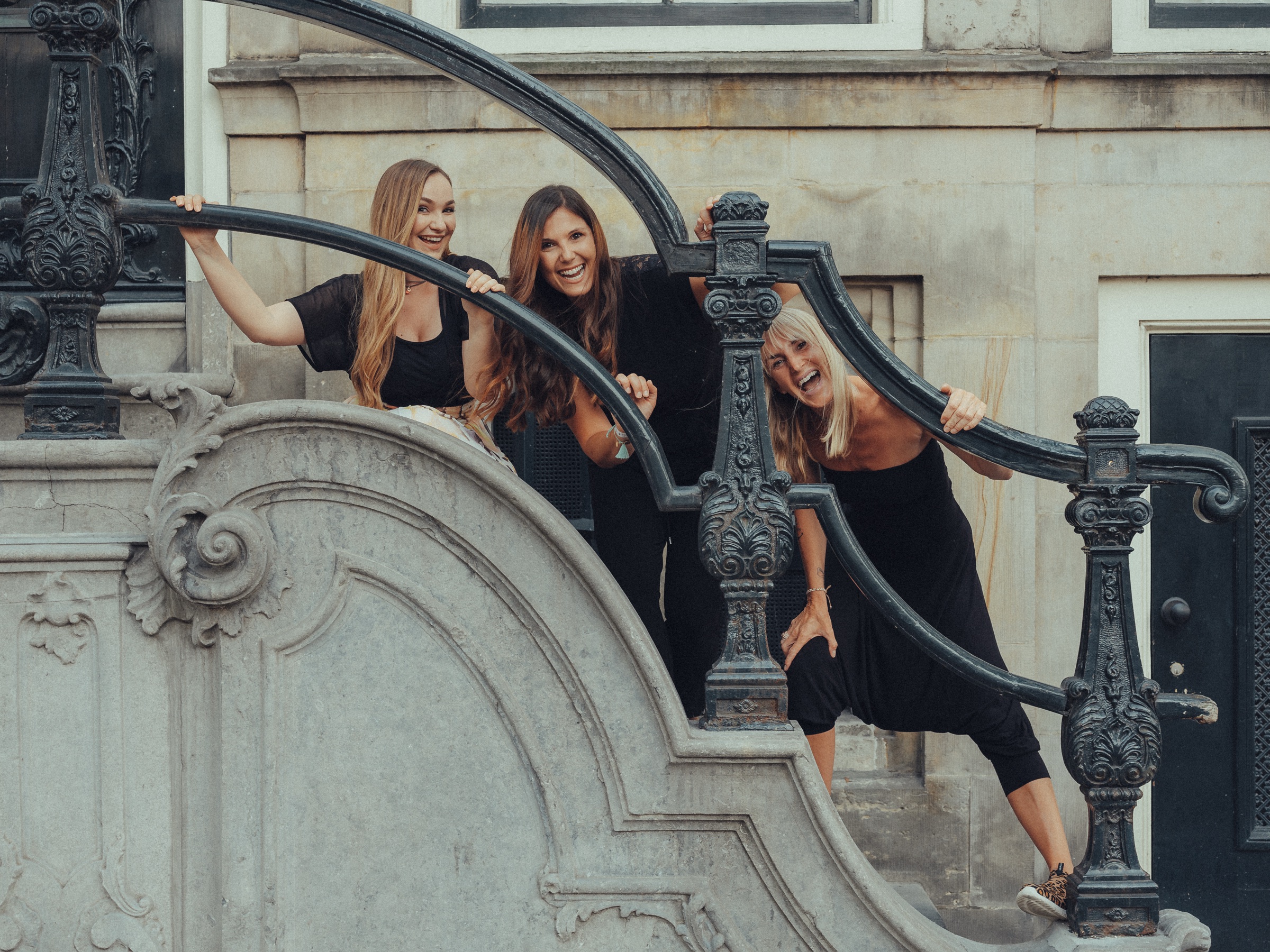 Three friends laughing through the curling iron railings of a grand stone stoop in front of an old canal house