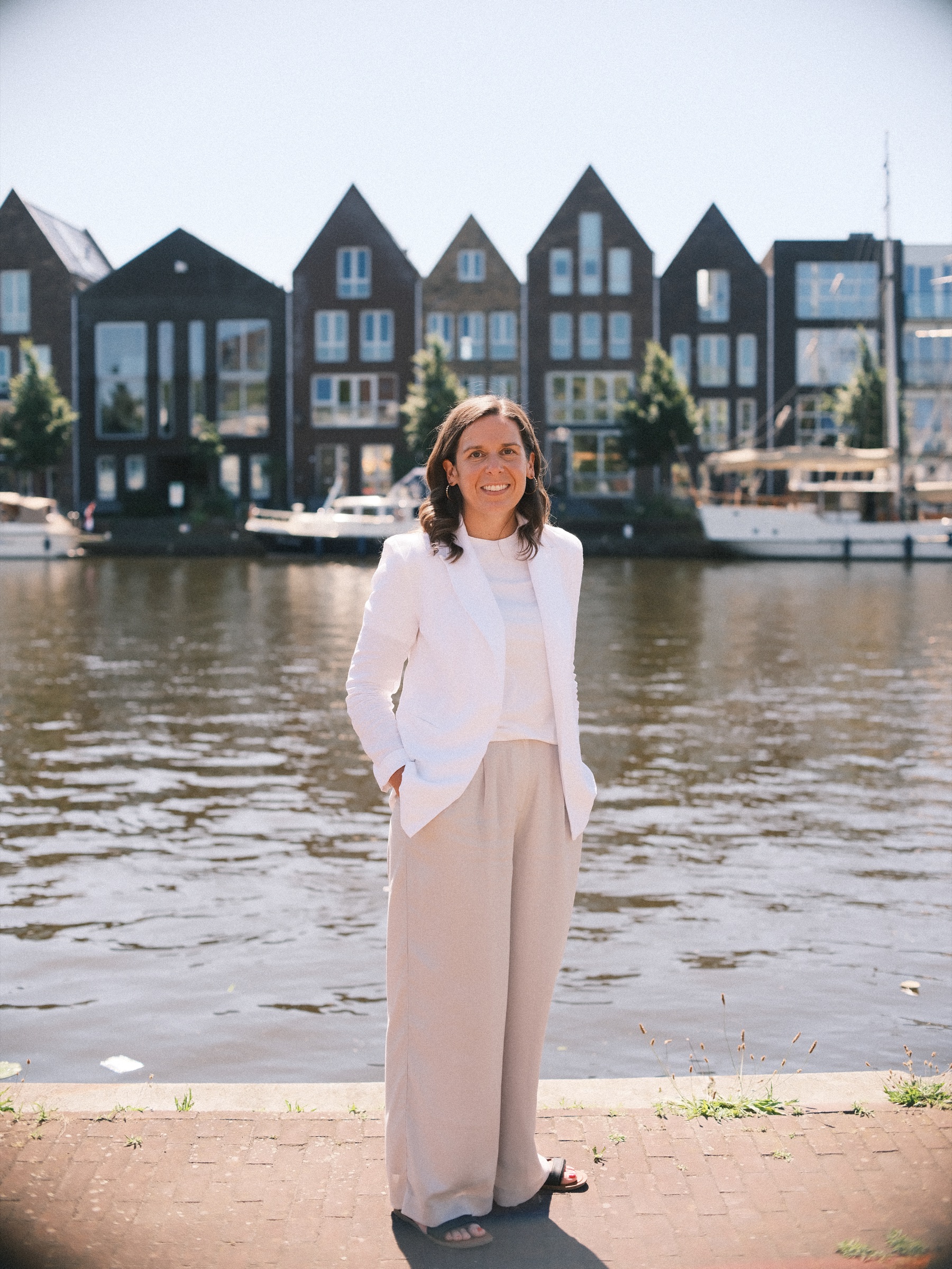 Vrouw in het wit staat aan de kade van het Spaarne, met zeilboten en nieuwe huizen met puntgevels aan de overkant