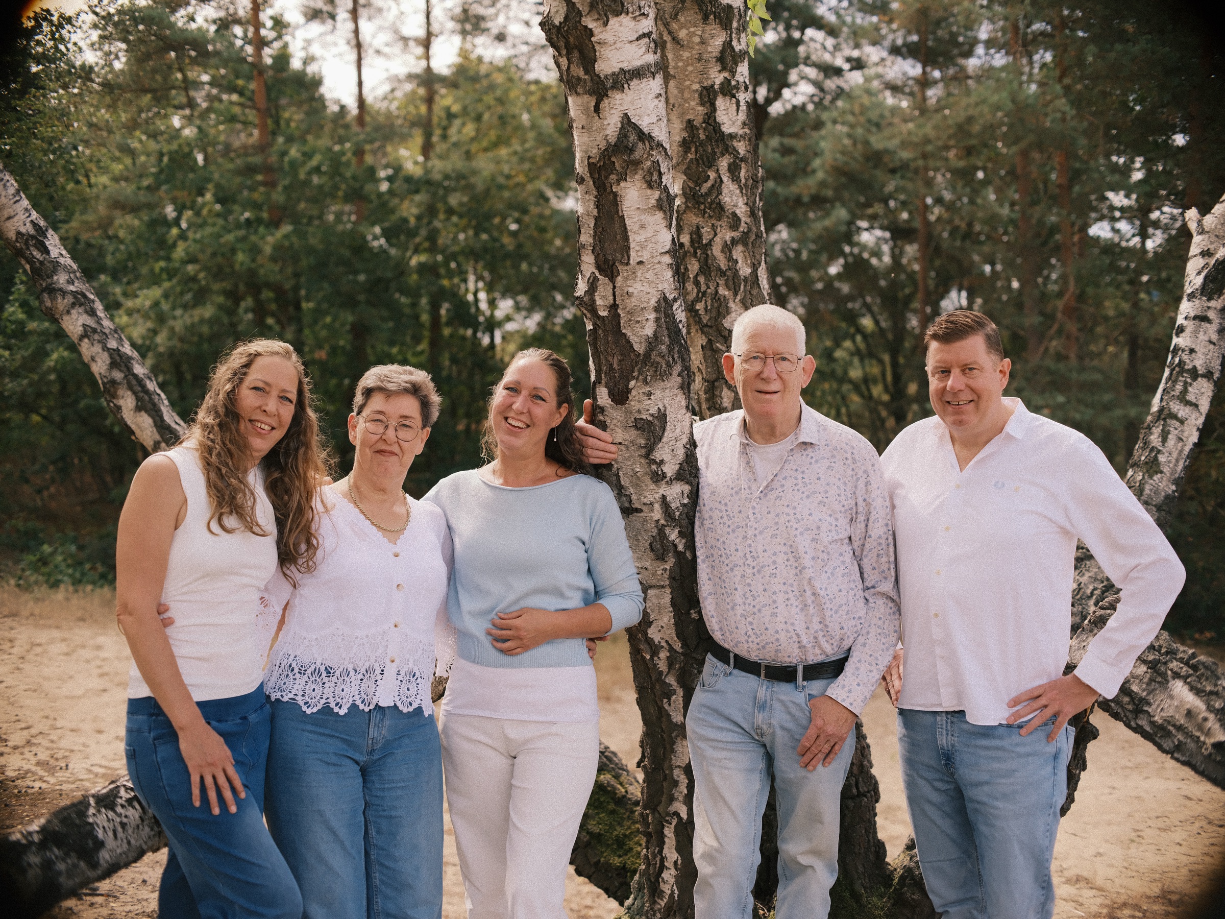 Grandparents with their three grown children under a crooked birch in the dunes, all smiling in white and soft blue