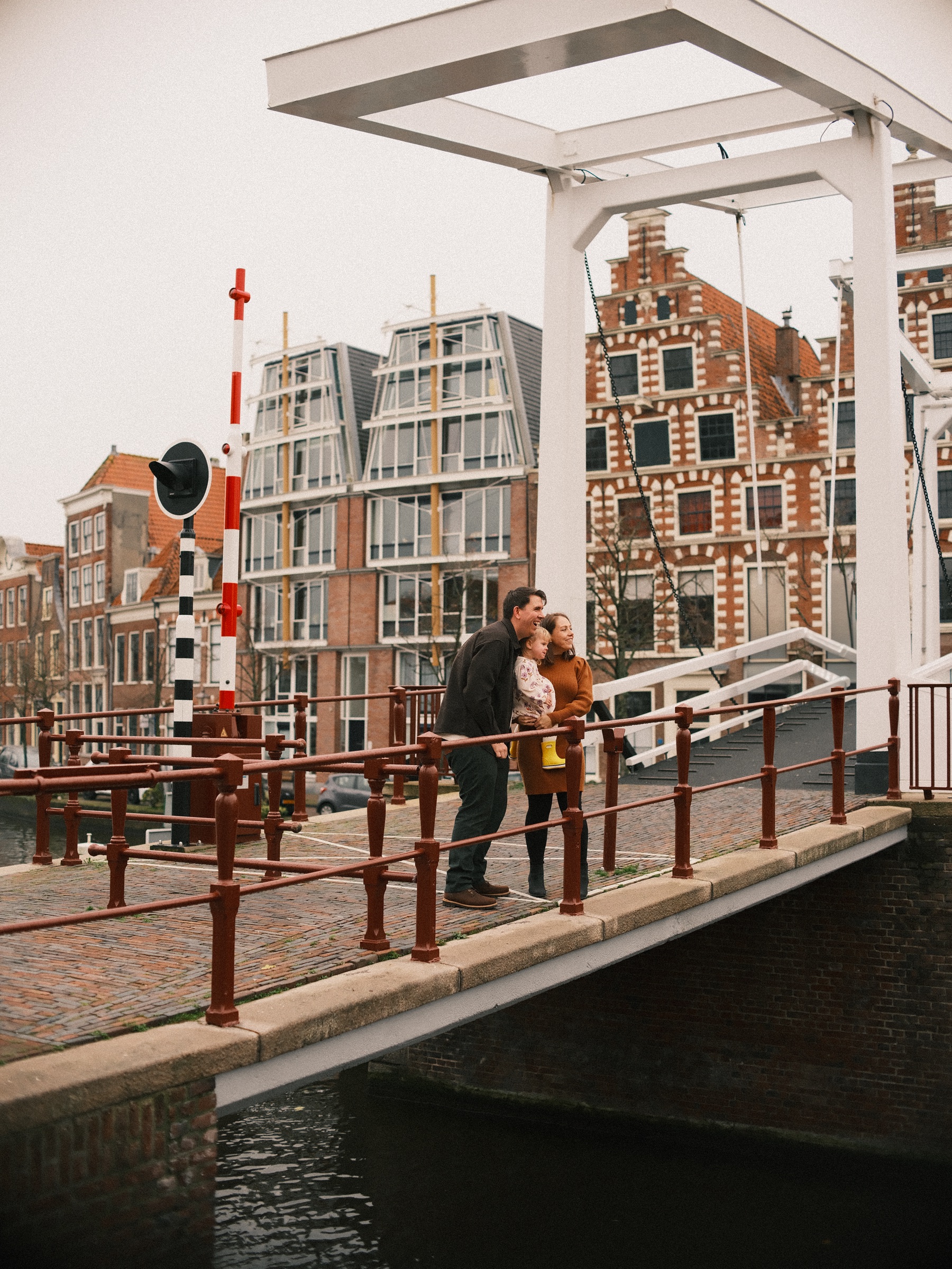 Witte ophaalbrug, de Gravestenenbrug, met roodbruine leuningen, een hoge trapgevel erachter en het gezin op de brug in november