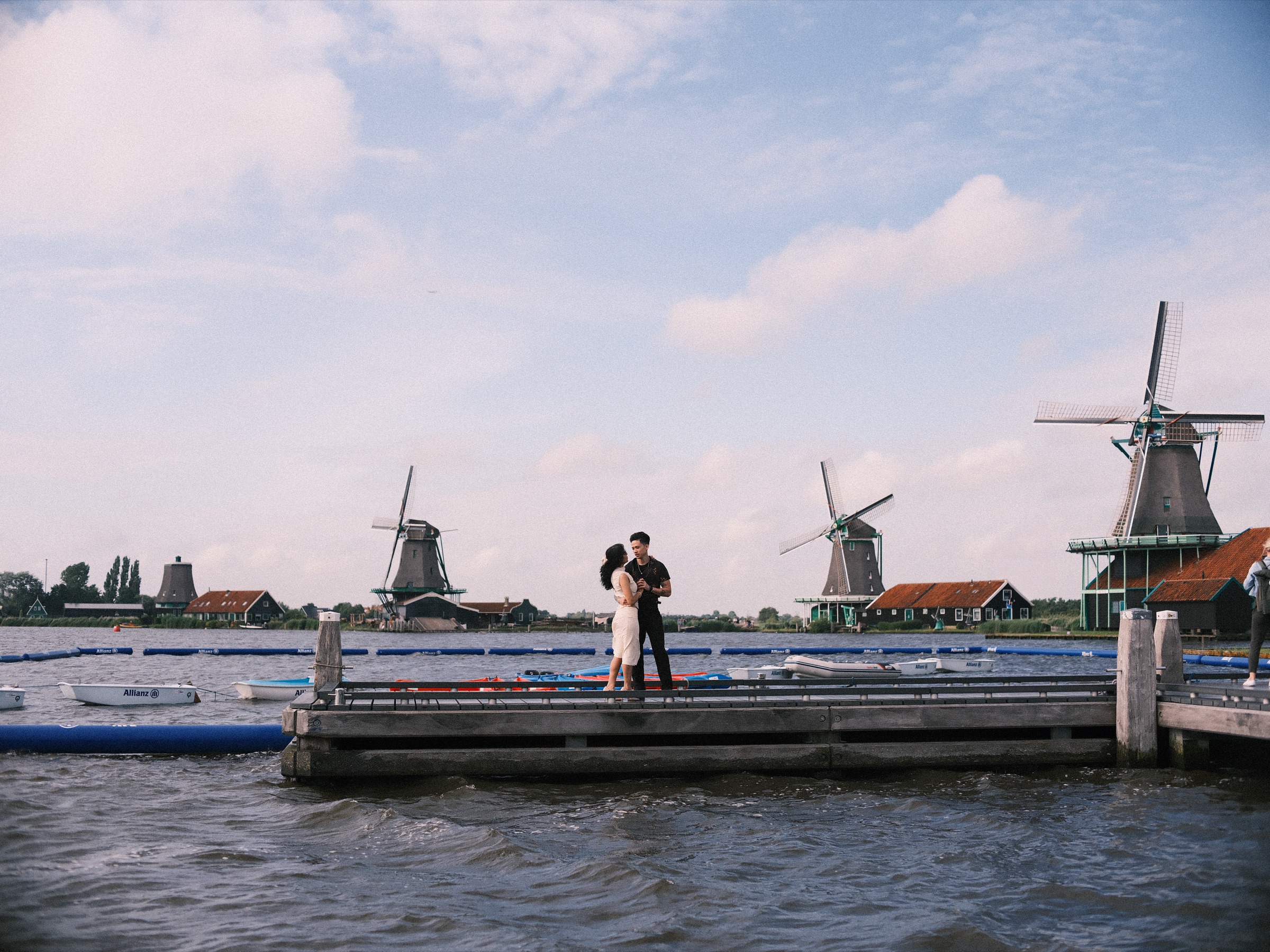 Couple kissing on a jetty over the Zaan under a blue sky with white clouds, the windmills of the Zaanse Schans on both sides
