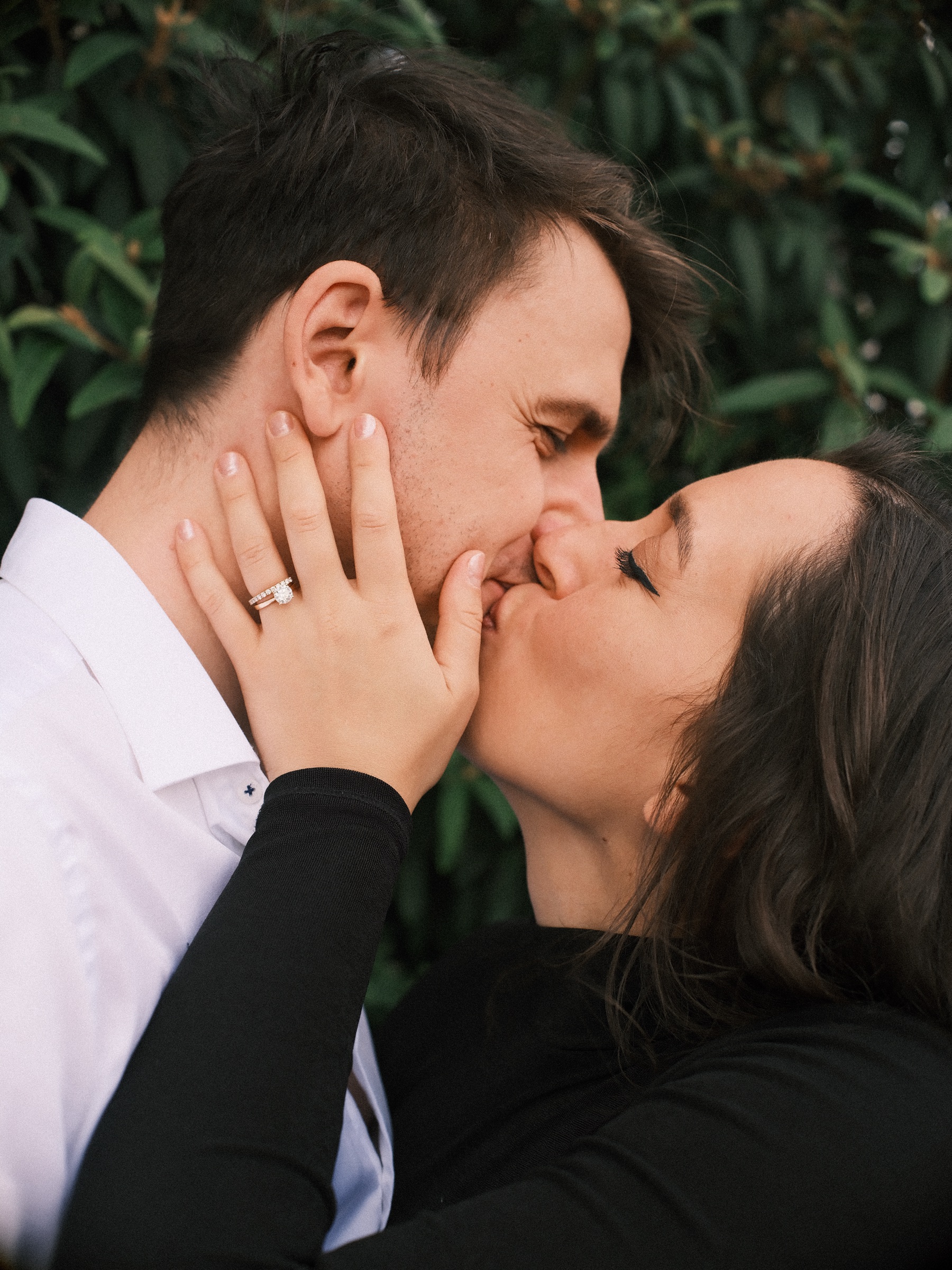 She holds his face and kisses him against a dark green hedge, her engagement ring in view, in the Scheepvaartkwartier of Rotterdam