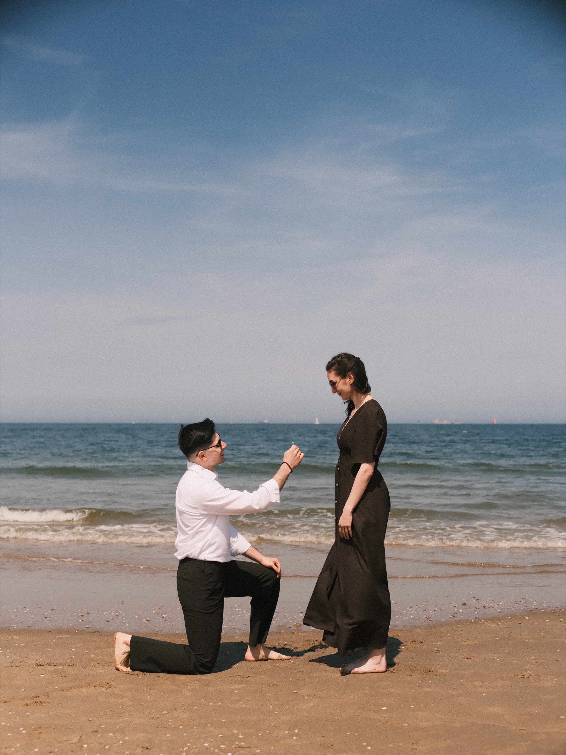 Barefoot in the sand, he kneels and holds out the ring as she smiles down at him by the sea, the surprise proposal on Scheveningen beach