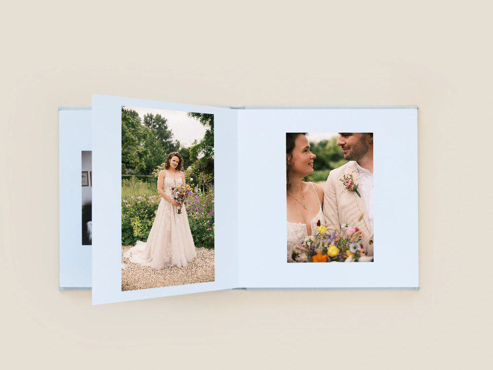 Open lay-flat photobook on a beige background, with a bride in a garden on the left page and the smiling couple with a bouquet on the right