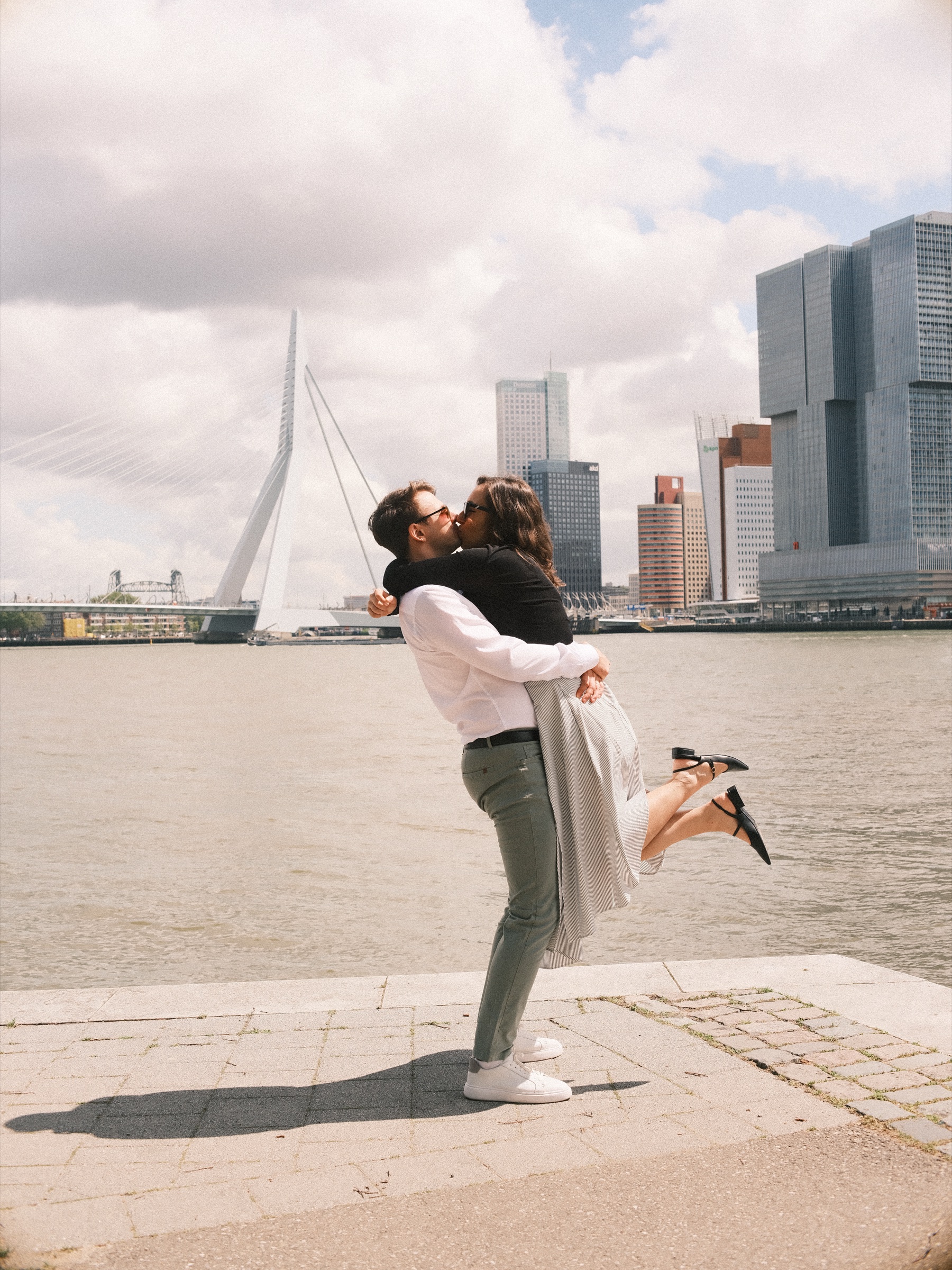 He lifts her off her feet and she kicks up one heel on the quay of the Maas, the Erasmusbrug and De Rotterdam behind them