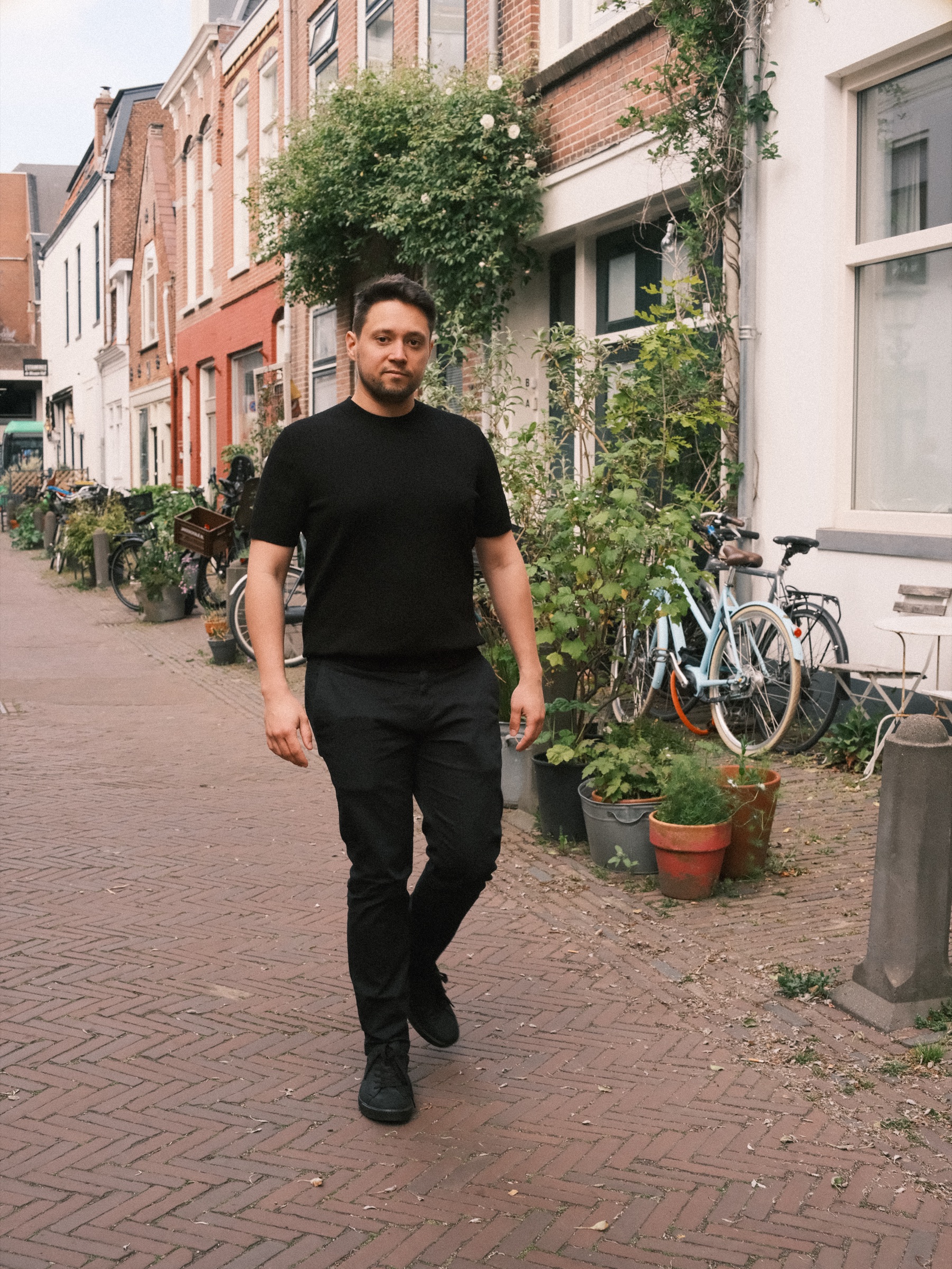 Man in een zwart T-shirt loopt door een smal klinkerstraatje in Haarlem, langs potplanten, fietsen en klimplanten tegen de oude gevels