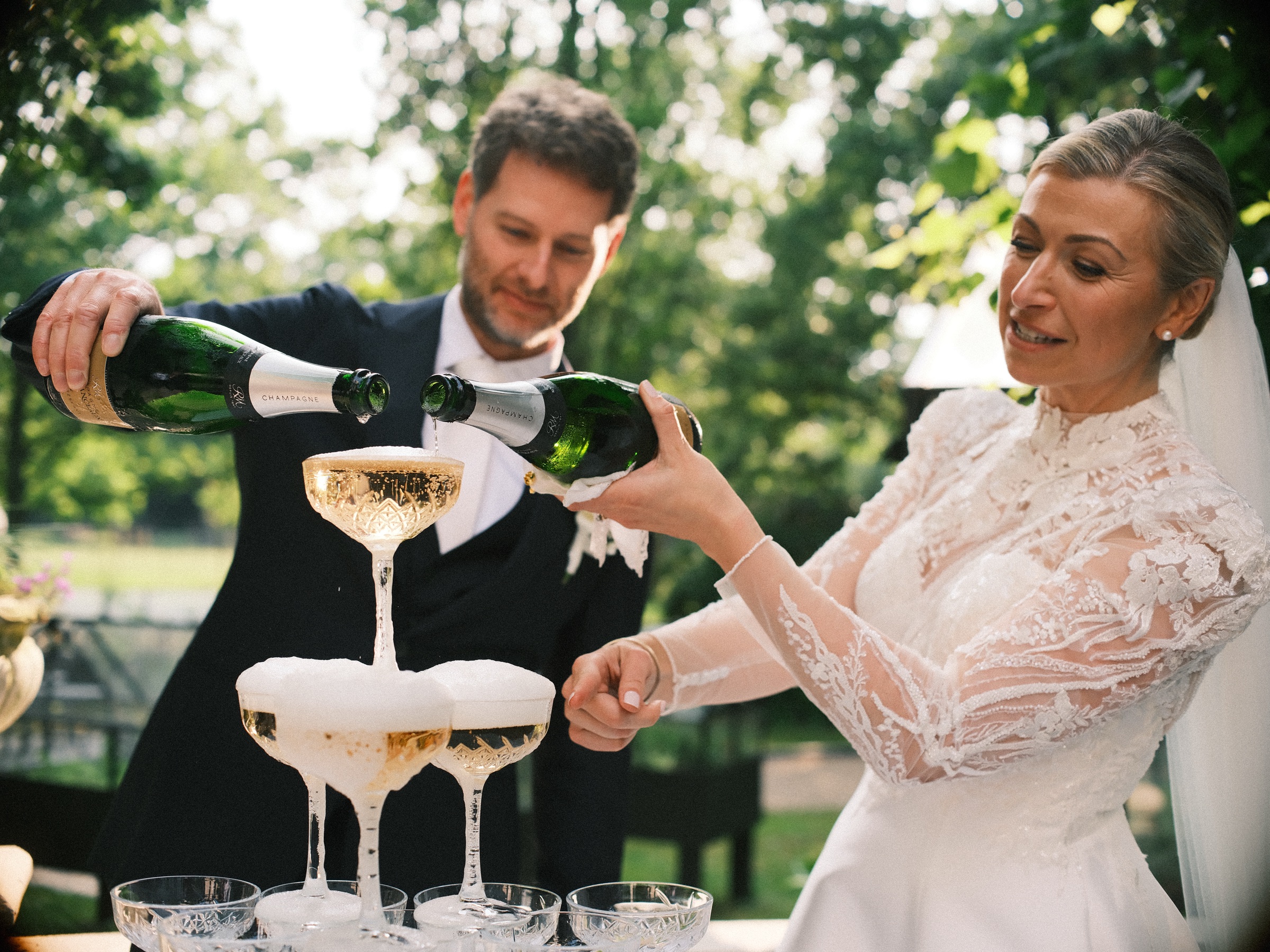 Het bruidspaar schenkt samen champagne in de bovenste coupe van de toren, terwijl het schuim over de randen loopt
