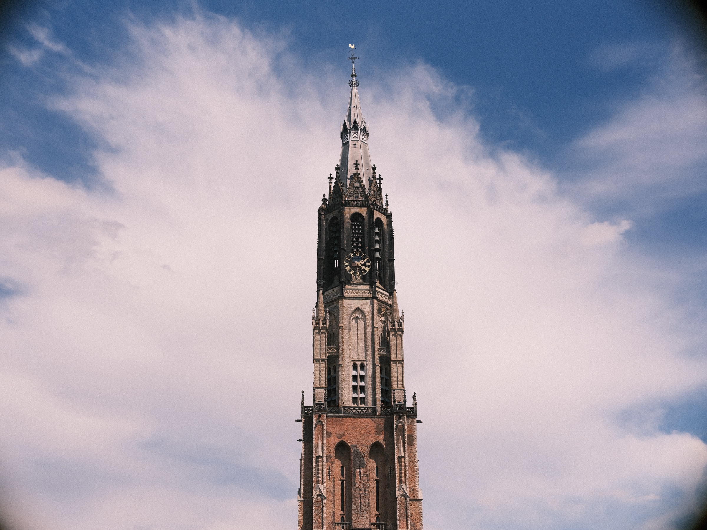 De toren van de Nieuwe Kerk steekt de diepblauwe lucht in, met een grote witte wolk die zich als een waaier erachter uitspreidt
