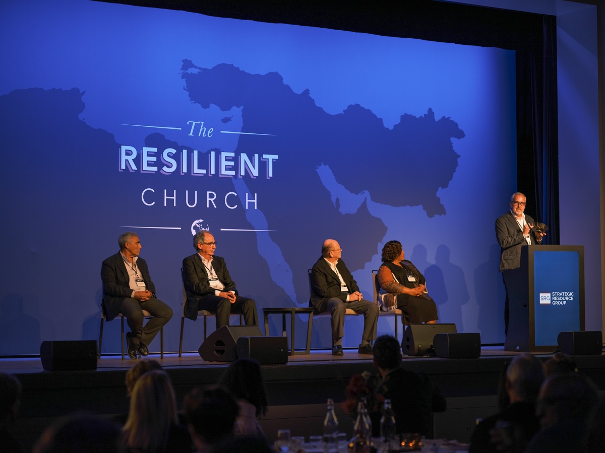 Panel van vier op het podium van de summit, met een gespreksleider achter het spreekgestoelte en een blauwe kaart van de regio