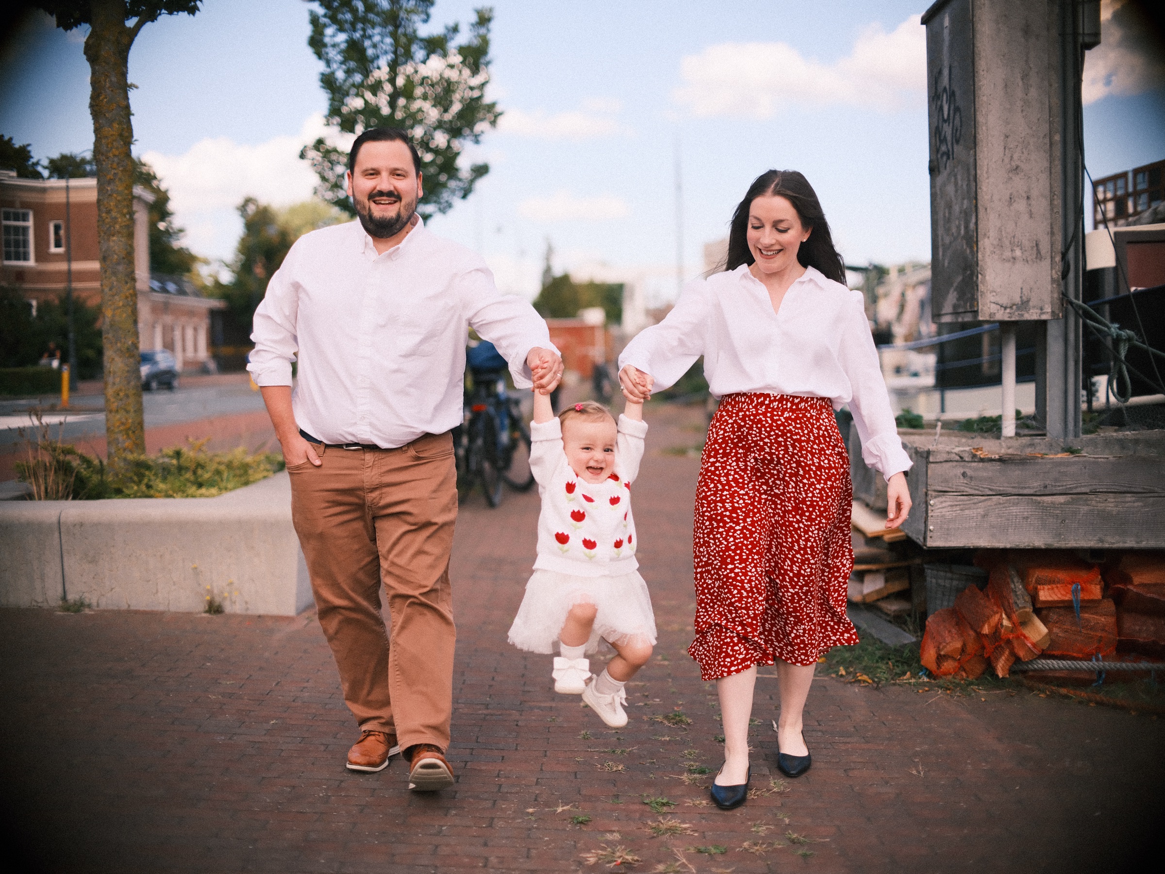 Ouders lopen over een kade in Haarlem en tillen hun dochtertje tussen twee stapjes aan haar handen op, met een boot erachter
