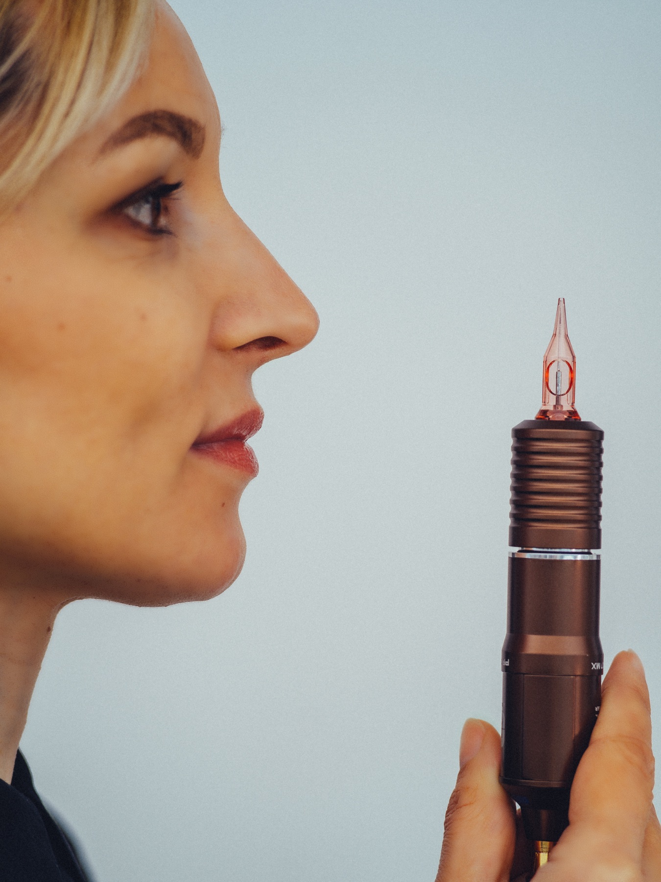 Specialist in permanente make-up houdt haar pen omhoog in profiel tegen een lichte muur, een beeld van de brandingshoot